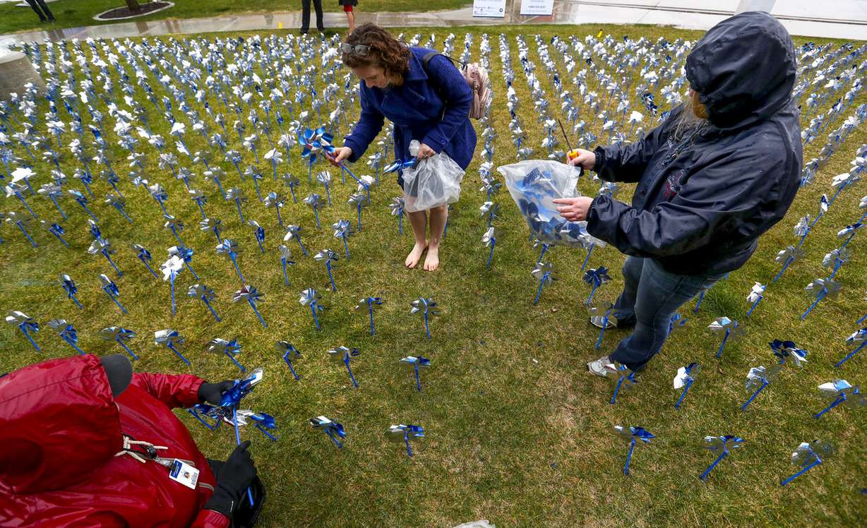 A barefoot Rebecca Virgo, program administrator for Prevent Child Abuse Utah's Parents as Teachers program, center, Carrie Jensen, with the Utah Attorney General’s Office and Children’s Justice Centers, right, and Dinah Weldon, director of the Center for Safe and Healthy Families at Primary Children’s Hospital, brave rain showers while helping place 1,720 pinwheels in the grass at Primary Children’s Hospital in Salt Lake City on Monday, April 15, 2019, as part of the “Pinwheels for Prevention” project. Virgo removed her high-heels because they were getting stuck in the soft grass. (Photo: Steve Griffin, KSL)