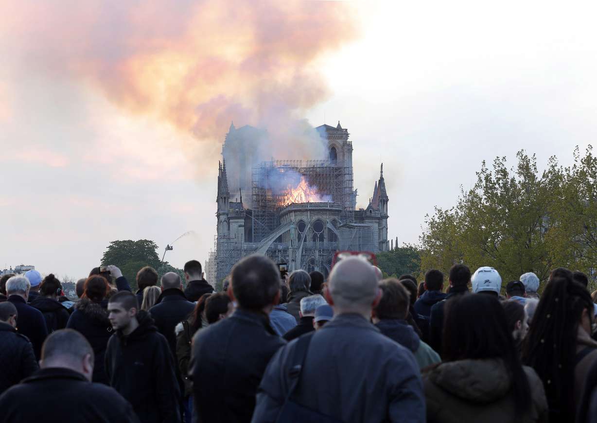 People watch as flames and smoke rise from Notre Dame cathedral as it burns in Paris, Monday, April 15, 2019. Massive plumes of yellow brown smoke is filling the air above Notre Dame Cathedral and ash is falling on tourists and others around the island that marks the center of Paris. (AP Photo/Thibault Camus)