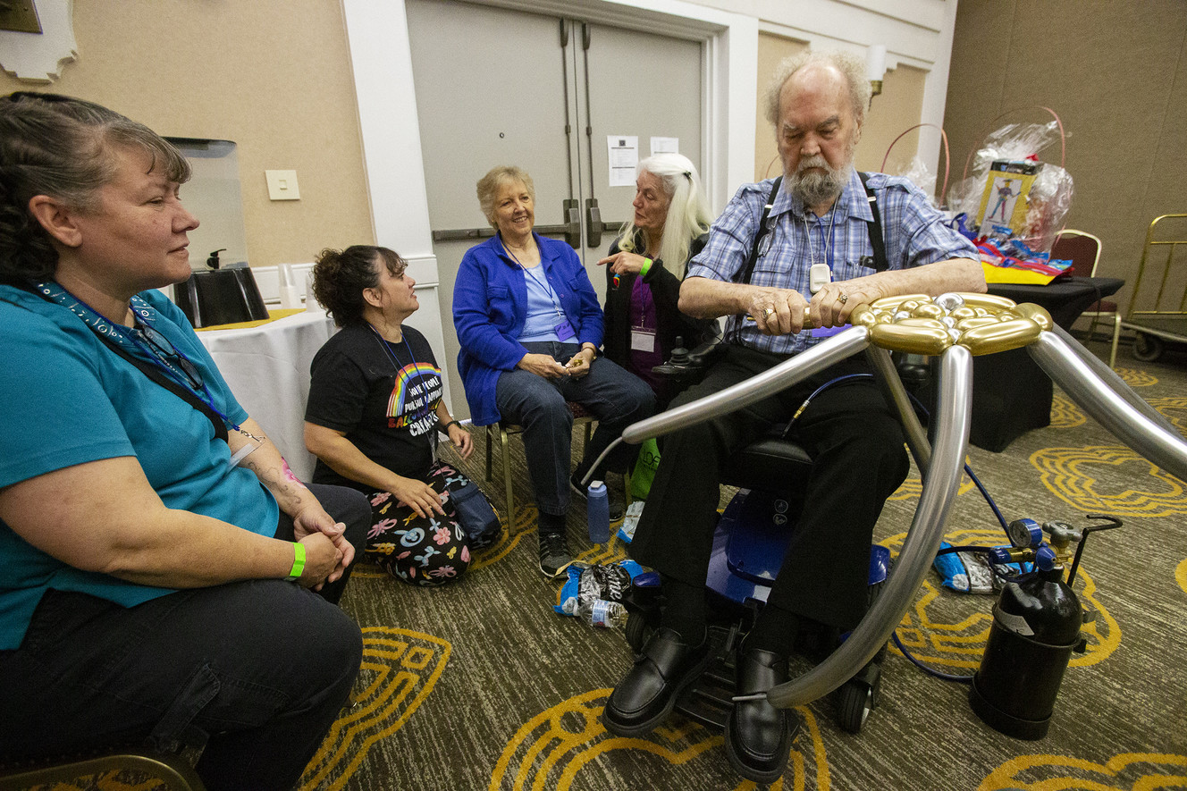 Sharon Neilson, of Salt Lake City, watches as Marvin Hardy works to make a top hat out of balloons while his wife Penny Hardy, who celebrated her birthday Monday, sits and talks with friends at a "Balloon Jam" at the Airport Doubletree Hotel by Hilton. Both Marvin and Penny Hardy are suffering from health troubles — Penny has stage 4 cancer that is in remission, and Marvin suffers complications from Agent Orange exposure during the Vietnam War — and fellow balloon artists are gathering in Salt Lake City to honor them. (Photo: Scott G Winterton, KSL)