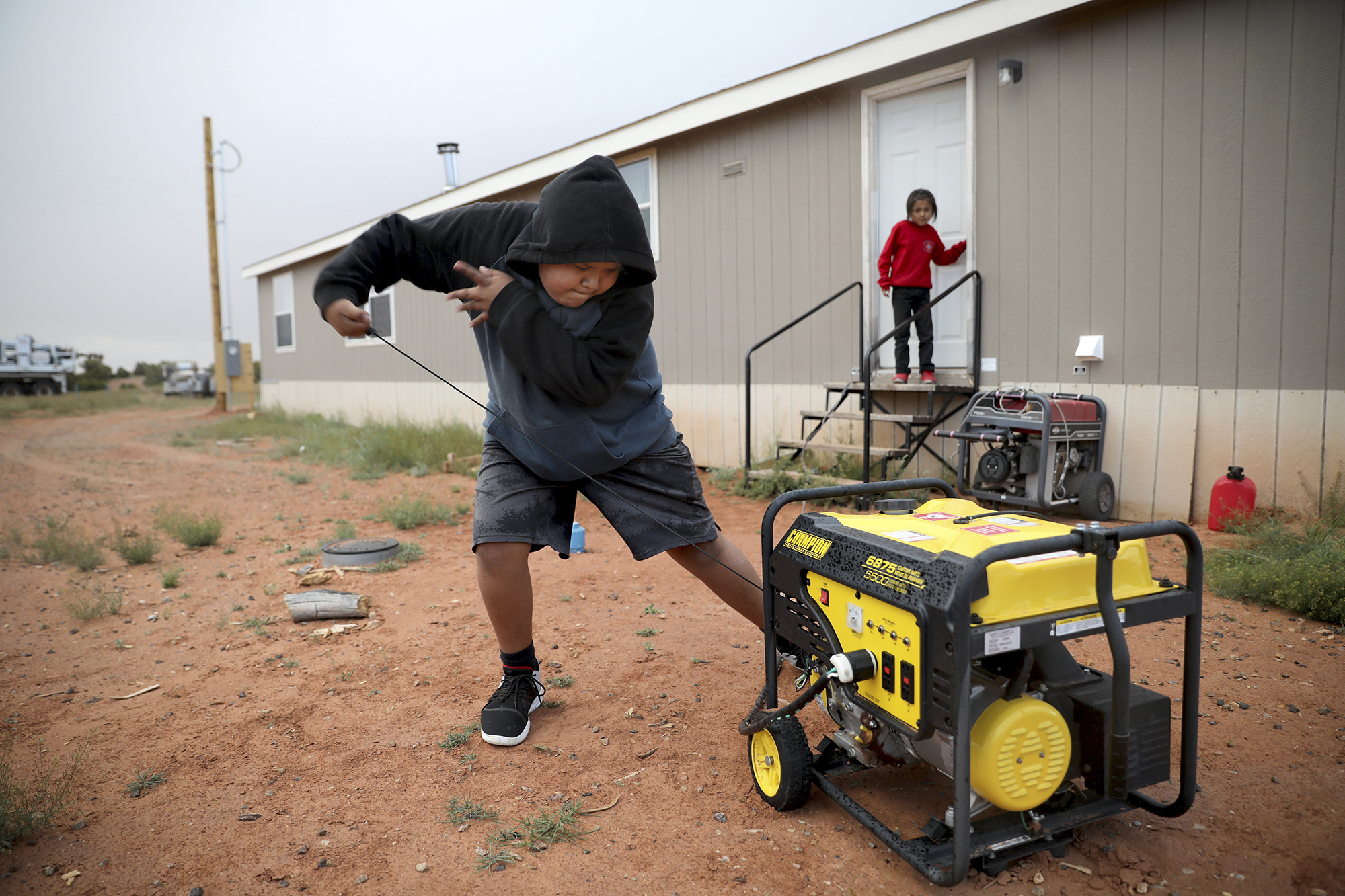 In this Wednesday, May 8, 2019 photo, Jayden Long, 13, starts the generator behind his Kaibeto home on the Navajo Reservation in Arizona, so that he can charge his cell phone inside the family home. (AP Photo/Jake Bacon)