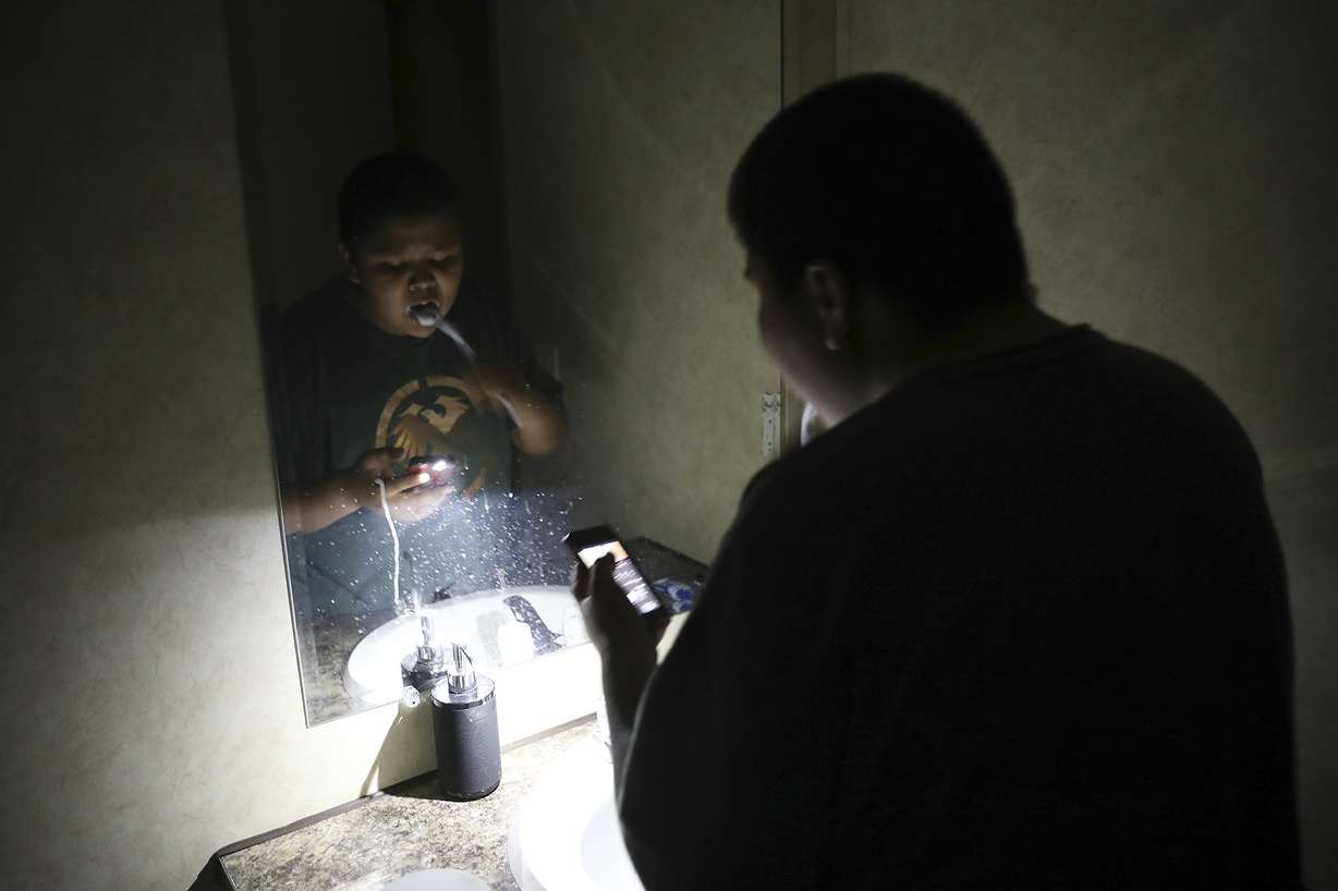 In this Wednesday, May 8, 2019 photo, Jayden Long, 13, brushes his teeth by cell phone light in the bathroom of his home on the Navajo Reservation. Long has spent more than a decade living with his family in a home with no electricity relying on a generator for power. (AP Photo/Jake Bacon)