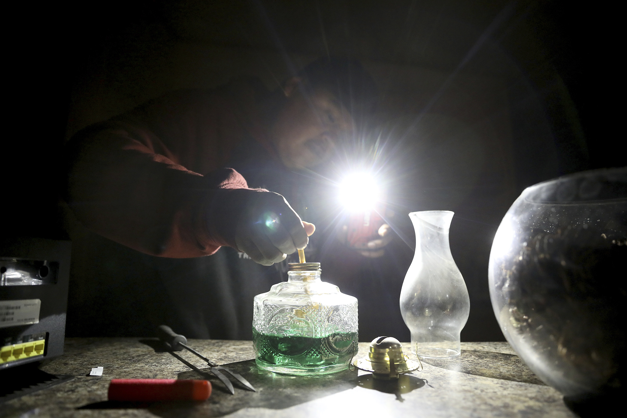 In this Wednesday, May 8, 2019 photo, Jimmie Long Jr. uses his cell phone flashlight to repair an oil lamp inside his Kaibwto home on the Navajo Reservation. Long and his wife, Miranda Haskie, were spending one last night without electricity in their home before being connected to the grid on Thursday, May 16, 2019. (AP Photo/Jake Bacon)