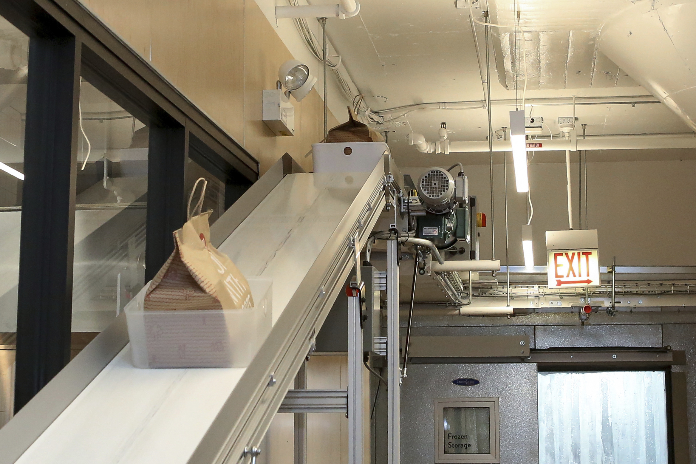A conveyor belt takes bags of food from ghost restaurants to a room where delivery drivers pick up orders at Kitchen United's Chicago location on Aug. 29, 2019. Kitchen United, a start-up that builds kitchen commissaries for restaurants looking to enter new markets through delivery or take-out only, has plans to open 40 more kitchens in cities across the U.S. through 2020. (Teresa Crawford, AP Photo)