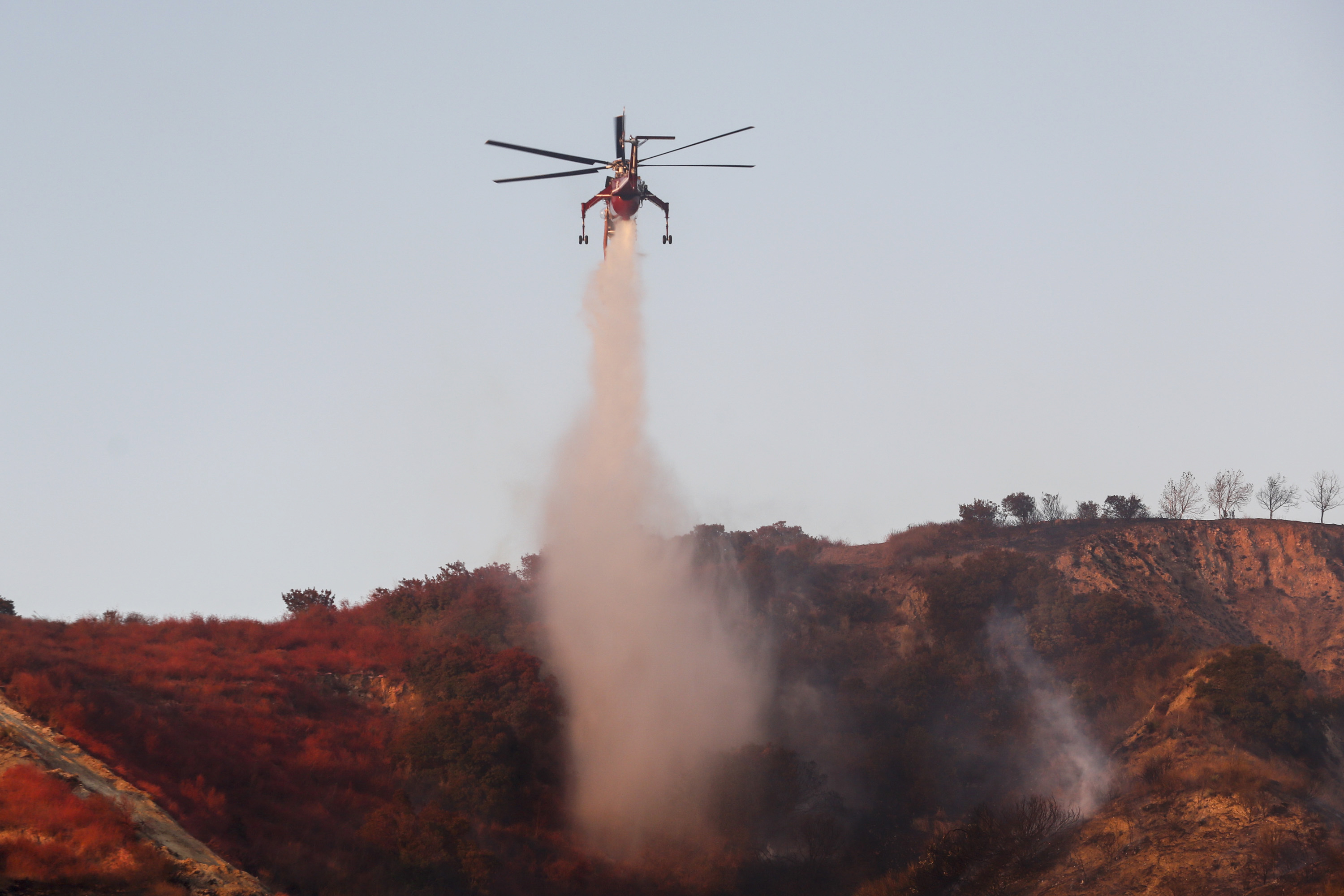 A helicopter drops water to put out hotspots in Simi Valley, Calif., Wednesday, Oct. 30, 2019. California is under siege at both ends of the state from fires, dangerous winds and deliberate blackouts. (AP Photo/Ringo H.W. Chiu)