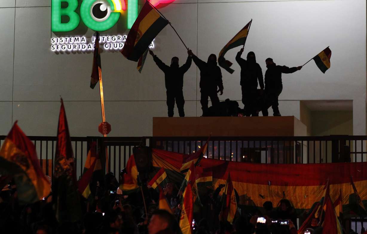 Police officers standing on the rooftop of a security booth at a police station wave Bolivian flags in front of protesters in La Paz, Bolivia, Saturday, Nov. 9, 2019. Growing dissension in police ranks posed a new threat to President Evo Morales, who claimed victory after the Oct. 20 vote but has since faced protests in which three people have been killed and hundreds injured. (Photo: Juan Karita, AP Photo.)