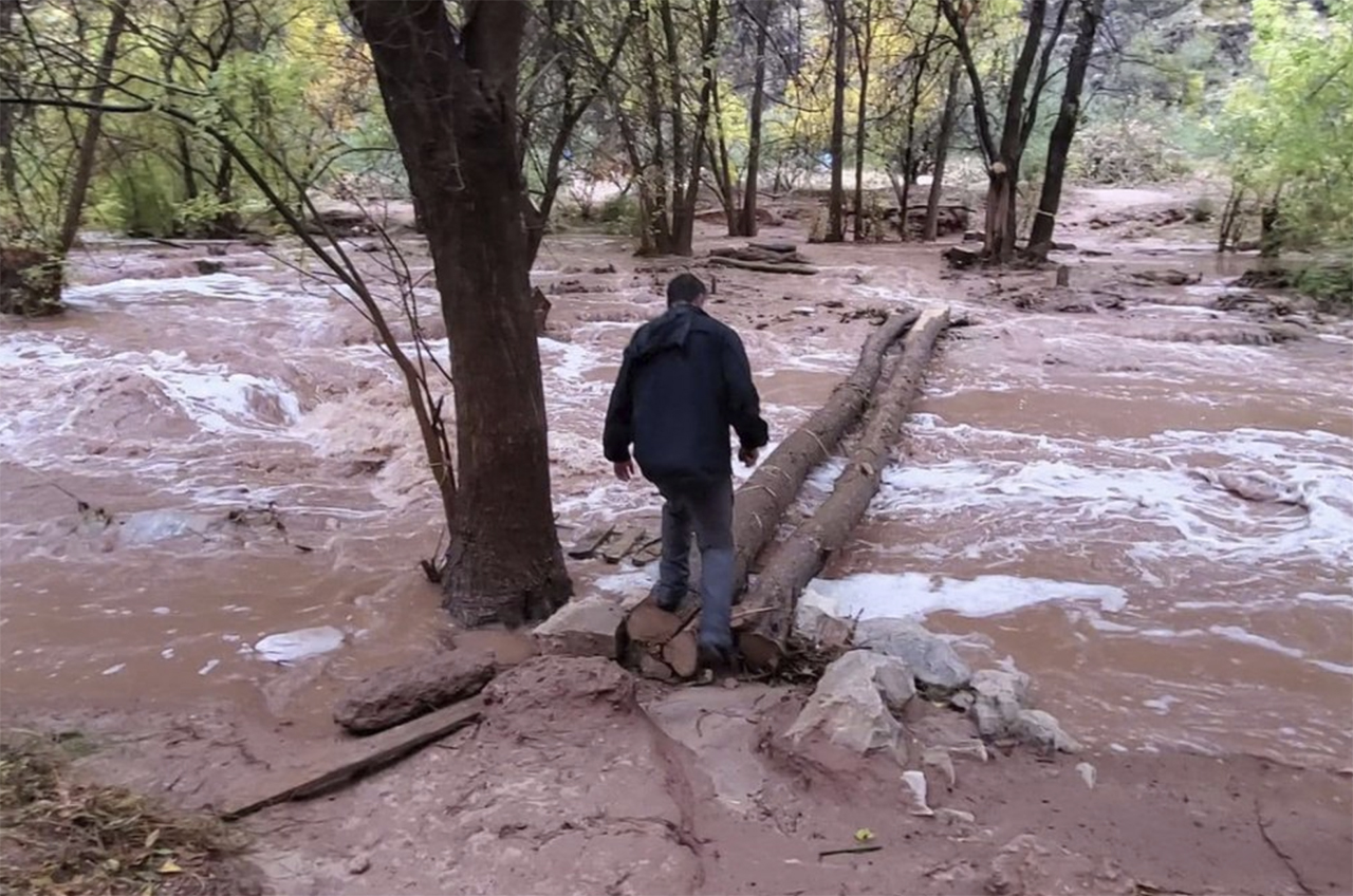 In this Nov. 29, 2019, photo, an unidentified man is seen crossing a flooded campground in Supai, Arizona. A popular tourist spot deep in a gorge off the Grand Canyon was flooded over the holiday, sending tourists scrambling to higher ground. The flood happened just days before the Havasupai Tribe shuts down its reservation to tourists for the season. No one was injured but some tourists woke up drenched and some lost camping gear. (Mandy Augustin via AP)