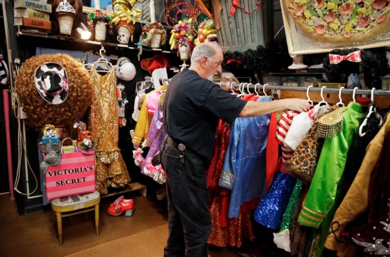 In this Tuesday, Nov. 19, 2019 photo, stage manager John Camajani looks through the numerous costumes hanging in the backstage dressing room of the musical "Beach Blanket Babylon" in San Francisco. The campy small San Francisco show that's been a must-see for tourists and locals alike for more than 45 years, making it the nation's longest continuously running musical revue, is closing its curtain. Its final performance is set for New Year’s Eve. (AP Photo/Eric Risberg)