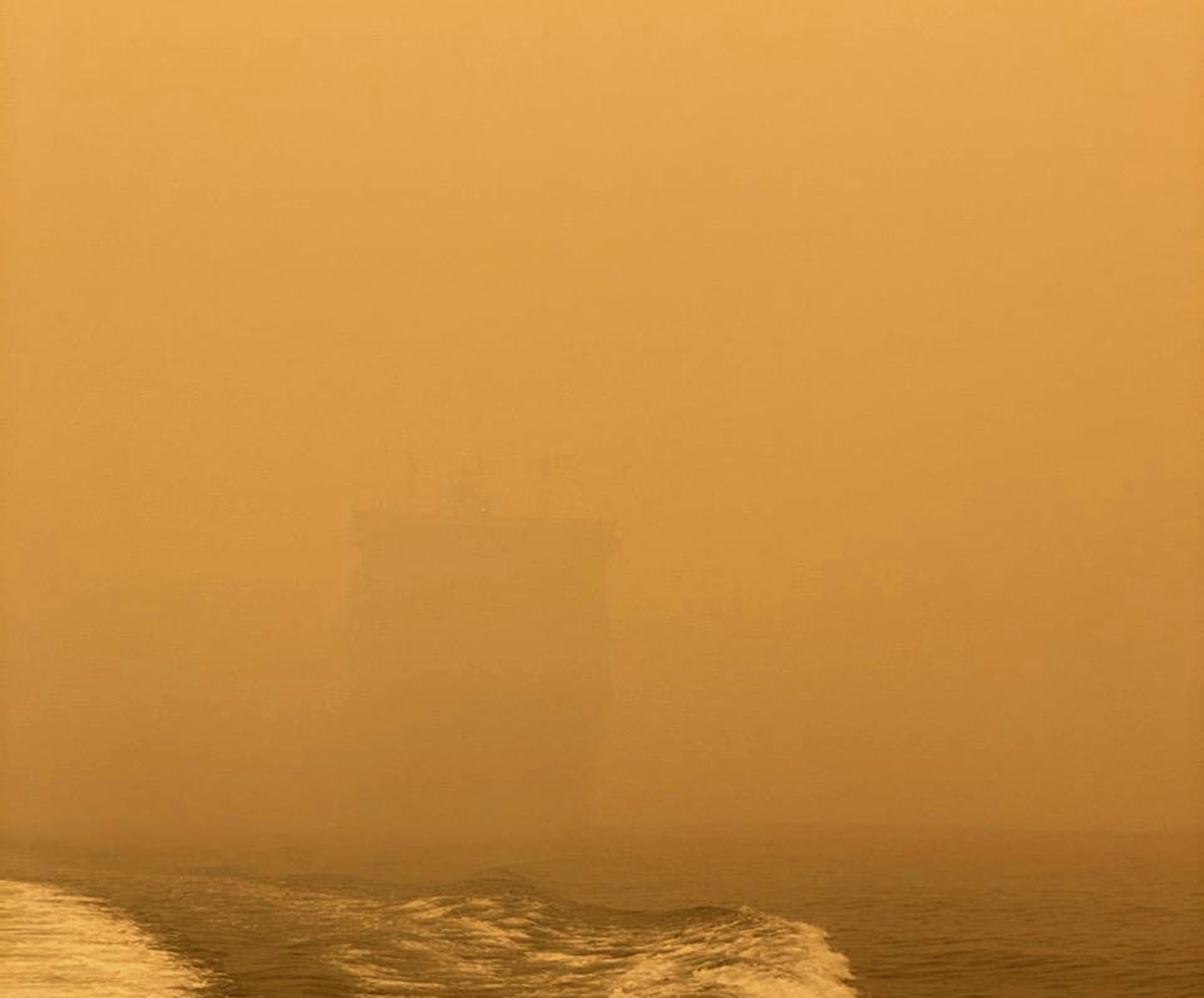 In this photo provided by the Australian Defence Force, HMAS Choules appears as a ghostly figure through smoke haze off the coast of Mallacoota, Australia, Thursday, Jan. 2, 2020. The Australian Defence Force is moving naval assets to Mallacoota on a supply mission that would last two weeks and helicopters would also fly in more firefighters since roads were inaccessible due to wildfires. (Australian Defence Force via AP)