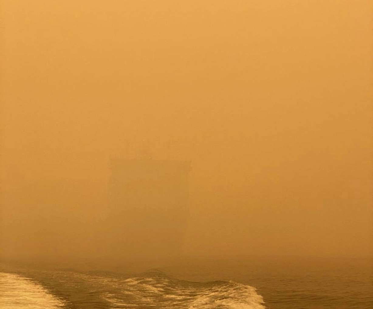 In this photo provided by the Australian Defence Force, HMAS Choules appears as a ghostly figure through smoke haze off the coast of Mallacoota, Australia, Thursday, Jan. 2, 2020. The Australian Defence Force is moving naval assets to Mallacoota on a supply mission that would last two weeks and helicopters would also fly in more firefighters since roads were inaccessible due to wildfires. (Australian Defence Force via AP)