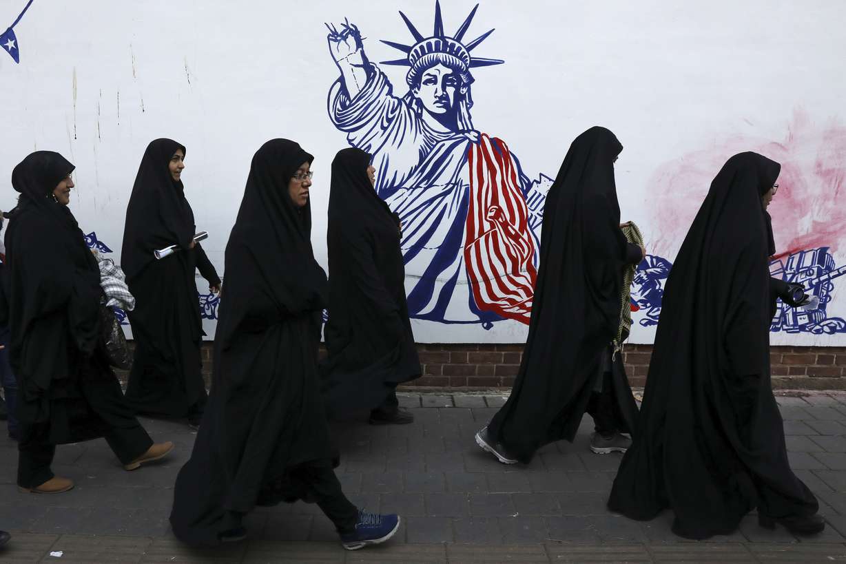 Mourners walk back from a funeral ceremony for Iranian Gen. Qassem Soleimani and his comrades, who were killed in Iraq in a U.S. drone attack on Friday, passing a satirical drawing of the Statue of Liberty painted on the wall of the former U.S. Embassy in Tehran, Iran, Monday, Jan. 6, 2020. (AP Photo/Vahid Salemi)
