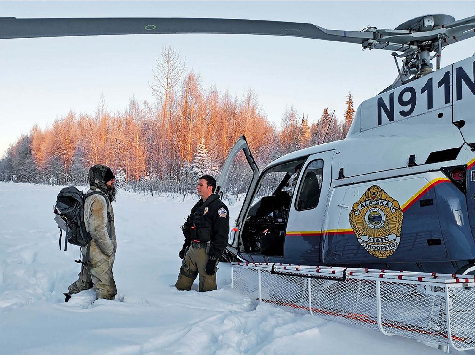 This Jan. 9, 2020 photo provided by Alaska State Troopers shows Tyson Steele, left, talking with Helo 3 Tactical Flight Officer Zac Johnson after Steele’s rescue outside Susitna Valley, Alaska. Troopers rescued Tyson Steele, 30, who survived in a makeshift shelter after his remote cabin burned last month, after spotting him and an SOS sign in the snow. (Photo: AP)