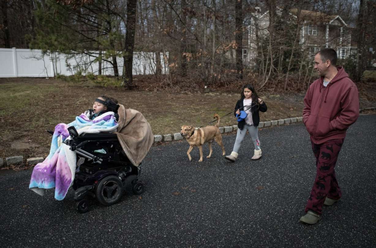 Jillian’s father, Jay, and sister, Samantha, join her for a walk. Jillian steers her wheelchair with her tongue, and a portable ventilator helps her breathe. (Kholood Eid via ProPublica)