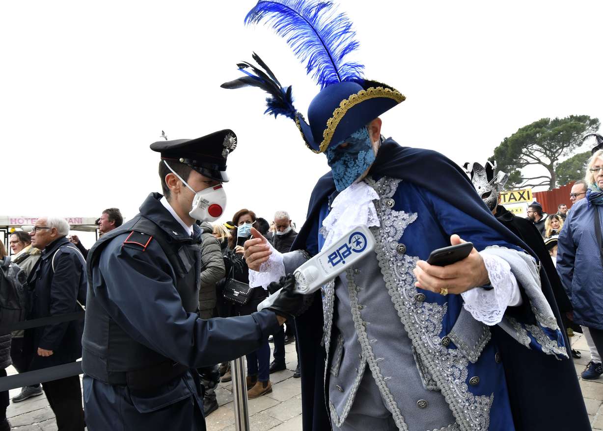 A policeman wearing a sanitary masks controls with a metal detector a reveler in Venice, Sunday, Feb. 23, 2020. Italian authorities have announced they are shutting down Venice's famed carnival events in a bid to stop the spread of the novel virus, as numbers of infected persons in the country have soared to at least 133, the largest amount of cases outside Asia. (Luigi Costantini, AP Photo)
