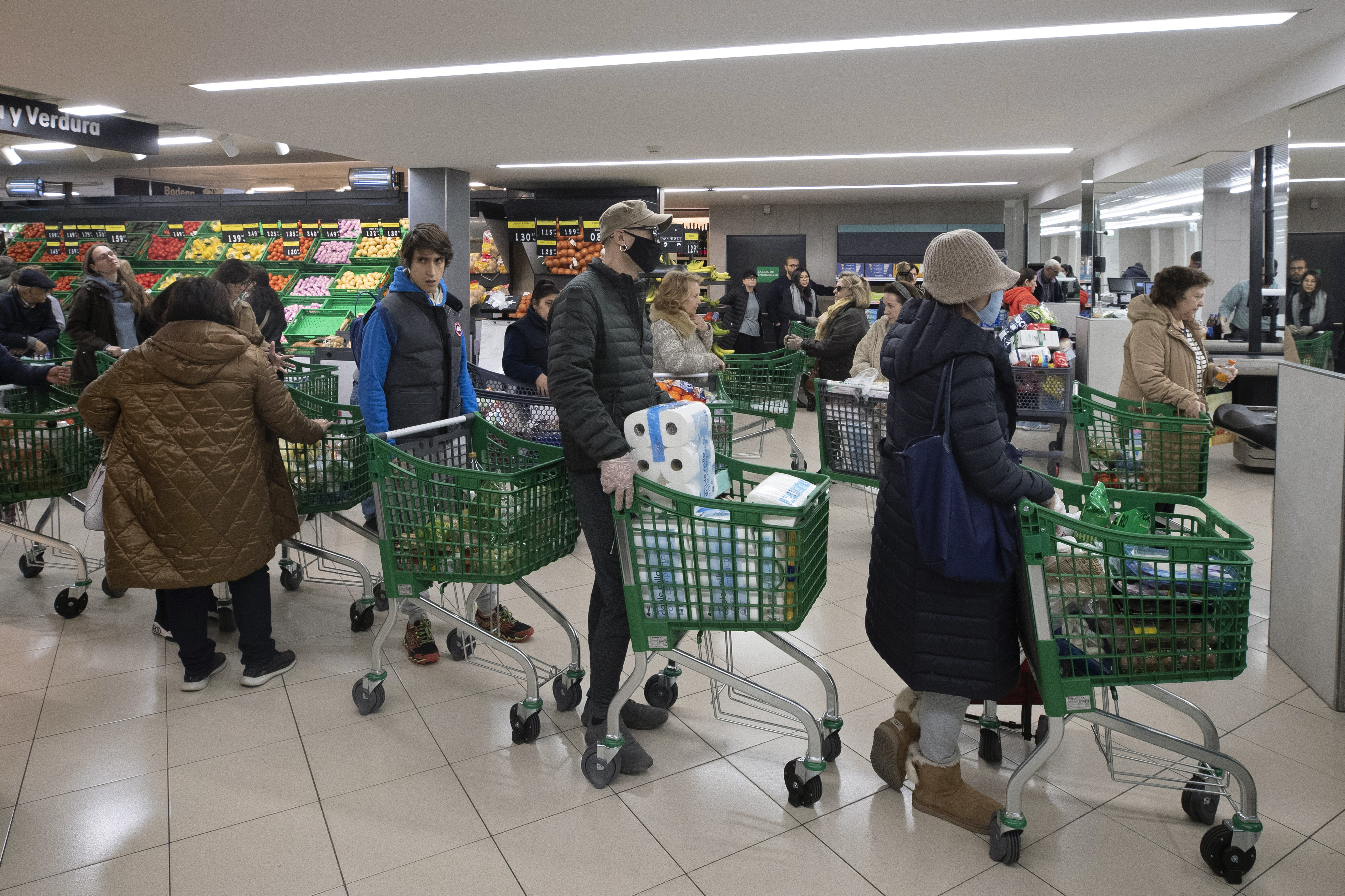 Customers, some with protective masks, queue at the check out of a supermarket as people begin to stock up on provisions in Madrid, Spain, Tuesday, March 10, 2020. (Paul White, AP Photo)