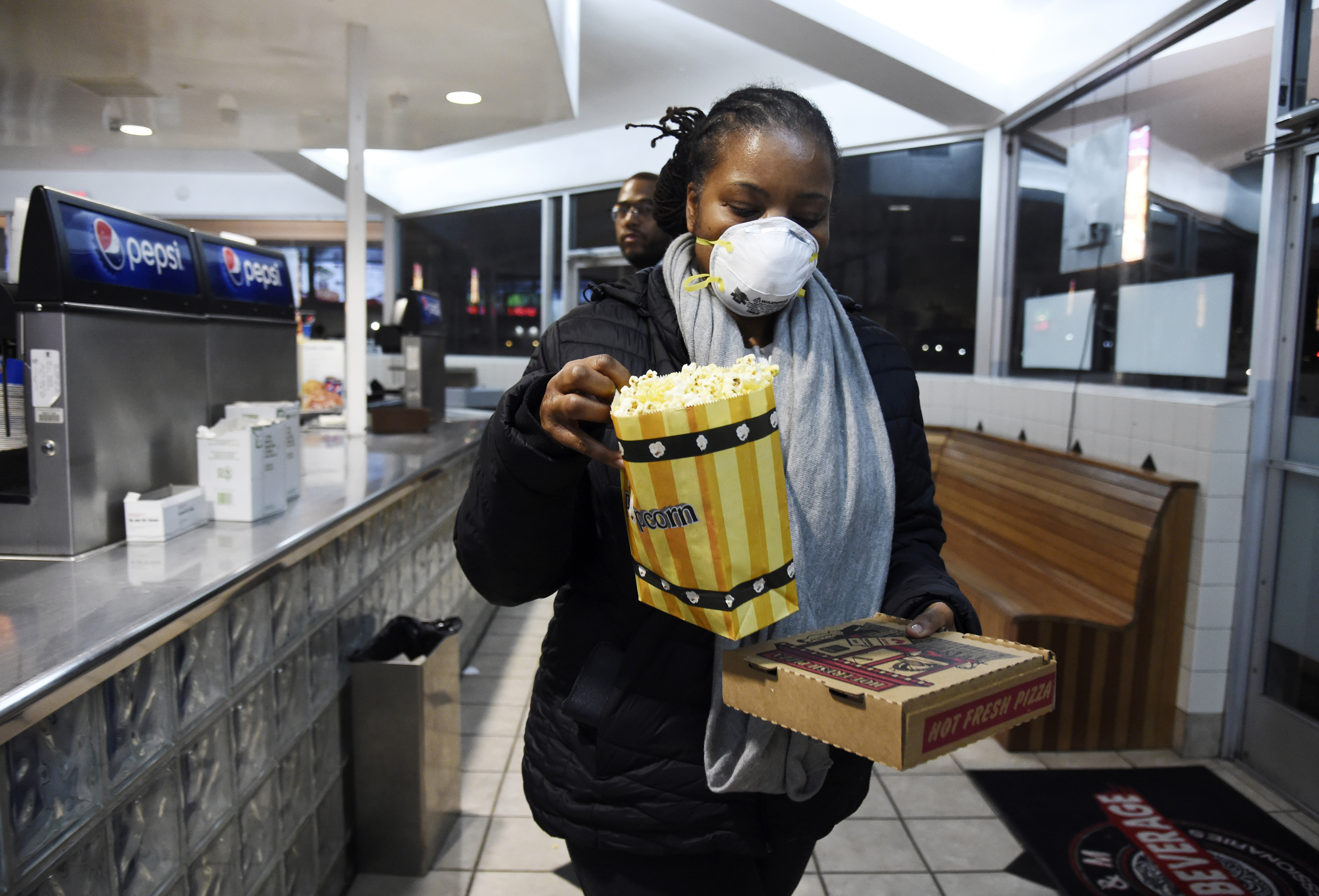 Andrea Wyatt of Inglewood, Calif., wears a mask as she collects her concessions at the Paramount Drive-In Theatres, Thursday, March 19, 2020, in Paramount, Calif. The drive-in theater, long a dwindling nostalgia act in a multiplex world, is experiencing a momentary return to prominence. With nearly all of the nation’s movie theaters shuttered due to the pandemic, some drive-in owners think they’re in a unique position to give moviegoers a chance to do something out of the house but stay within prudent distance from one another. (AP Photo/Chris Pizzello)