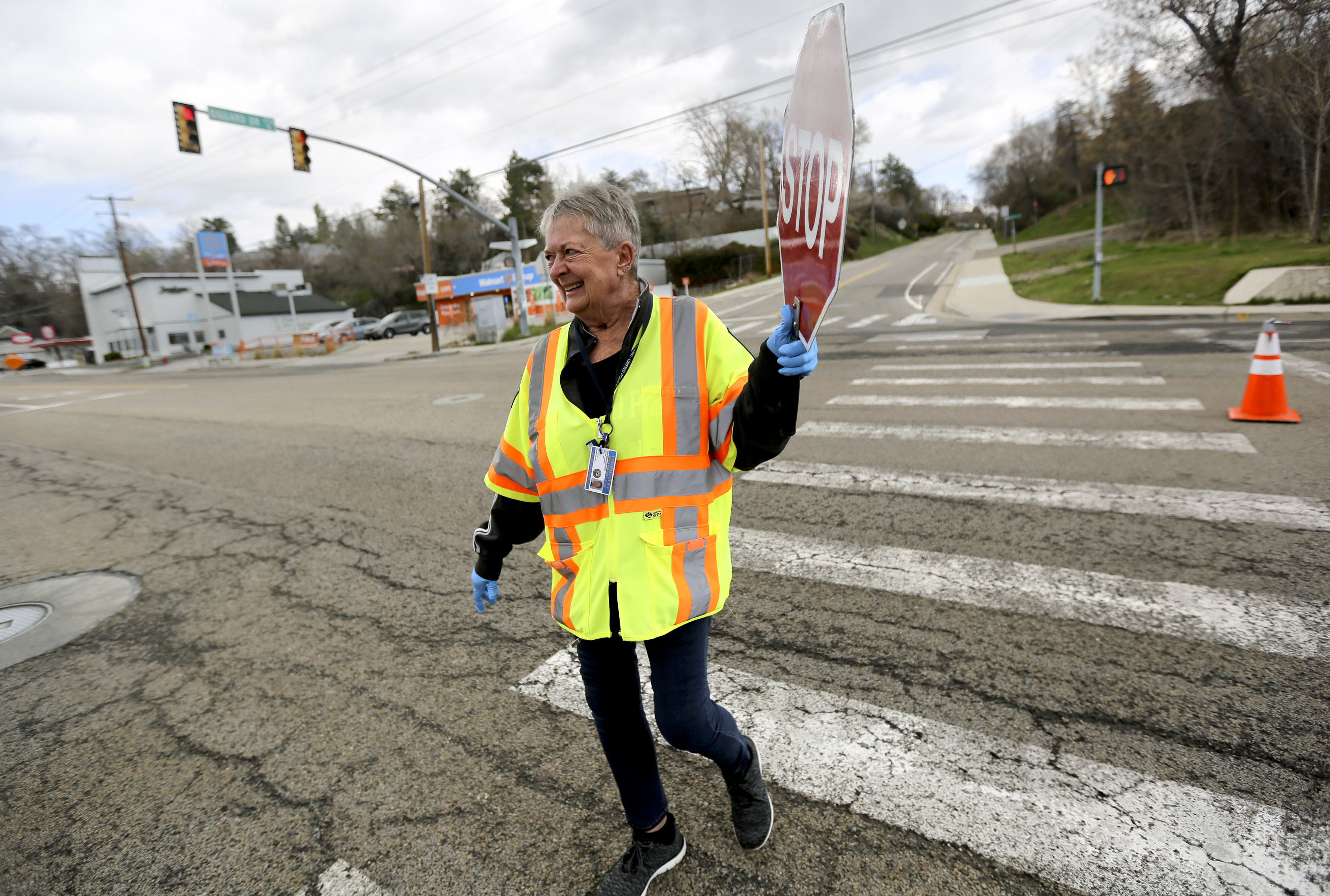 Nelda Wiberg walks back to the sidewalk after helping students cross Highland Drive in Millcreek on Tuesday, March 31, 2020. Schools are closed due to COVID-19, but crossing guards still help students if they need to walk to school to get homework supplies or lunch. (Kristin Murphy, KSL)