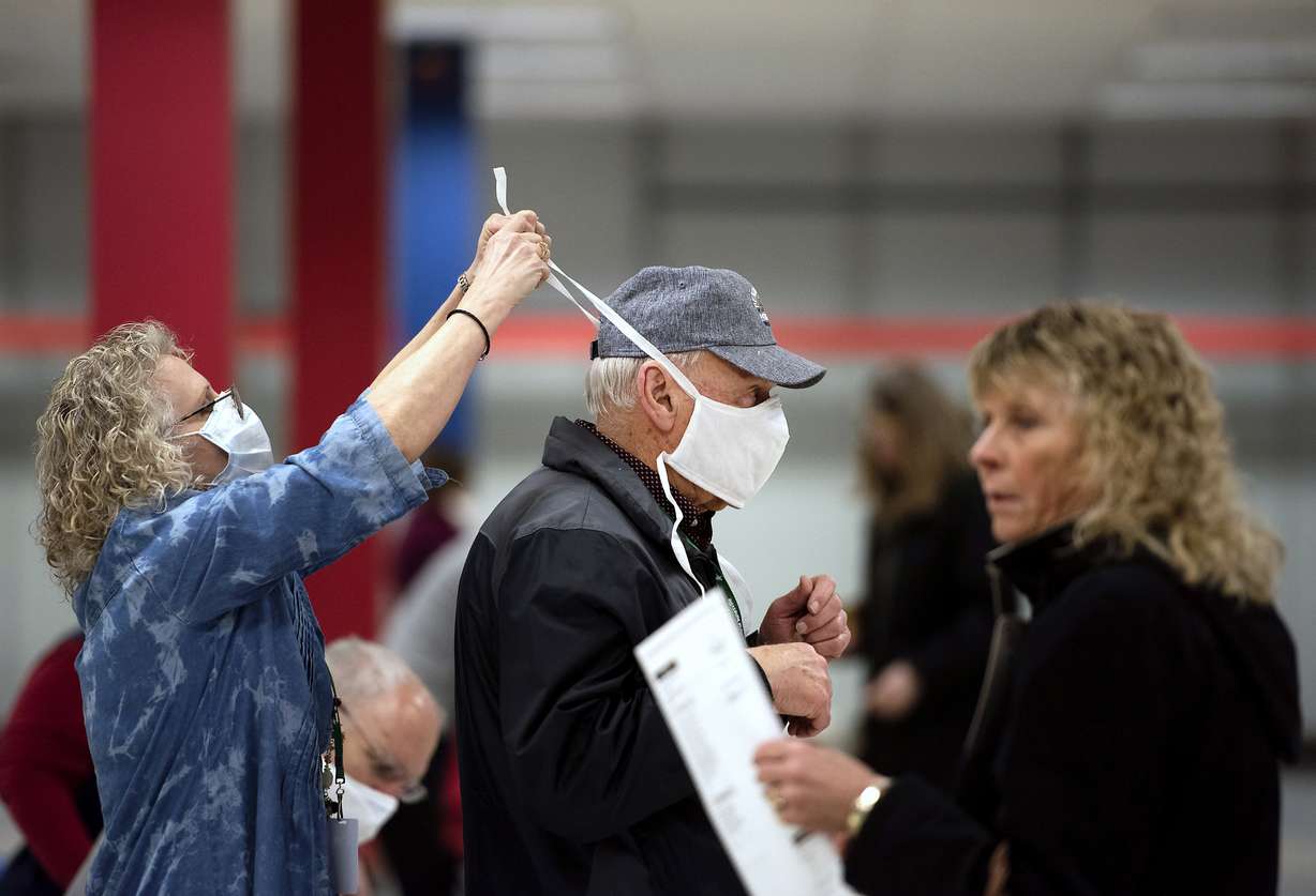 Poll worker Patty Piek-Groth, left, helps fellow poll worker Jerry Moore, center, put on a mask to prevent the spread of coronavirus, as the polls open for the presidential primary election at the Janesville Mall in Janesville, Wis., on Tuesday, April 7, 2020. (Angela Major/The Janesville Gazette via AP)