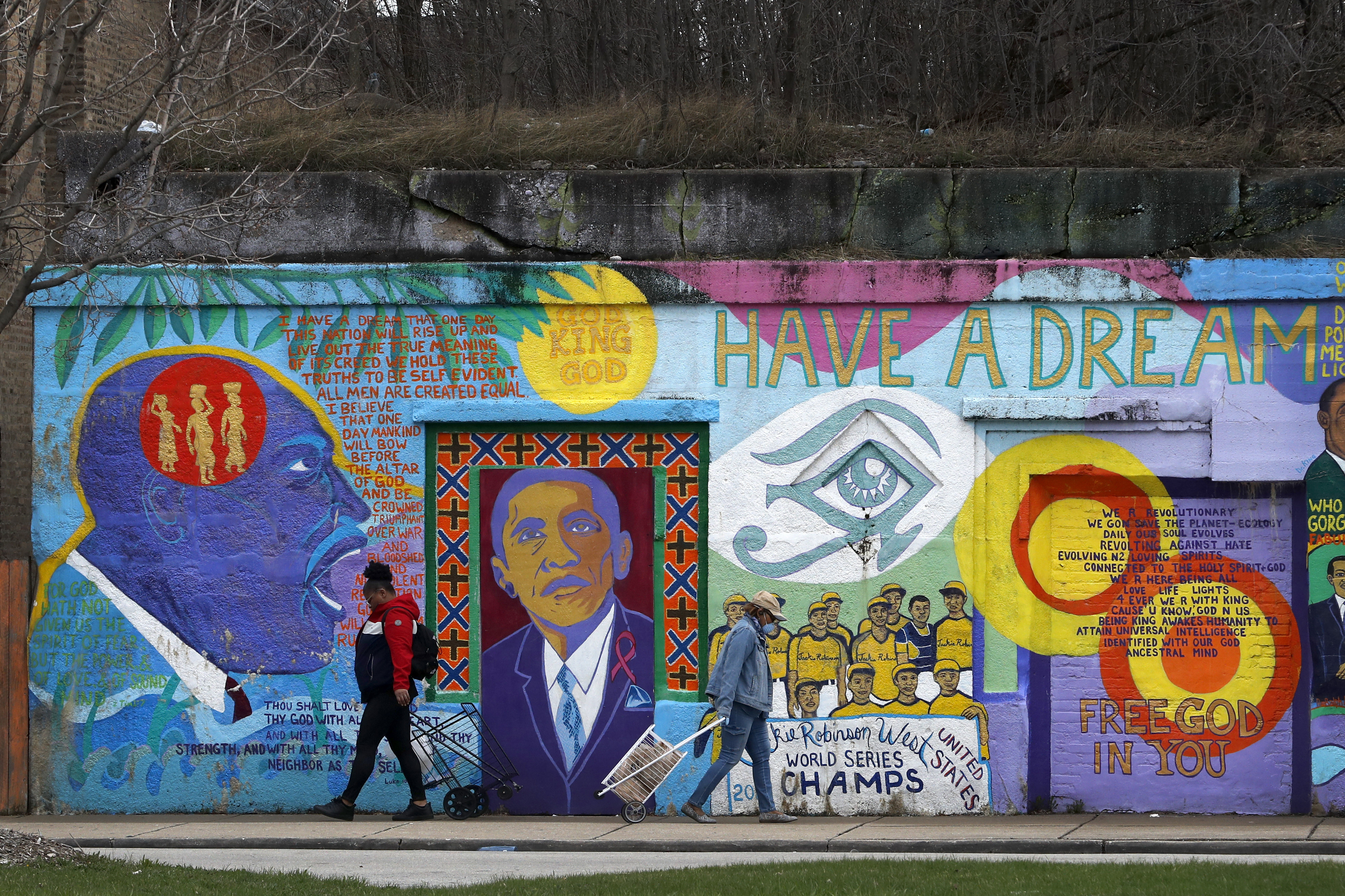 In this April 7, 2020, photo, two women pass each other and an African-American mural as they travel to and from a local grocery store on Chicago's Southside. As the coronavirus tightened its grip across the country, it is cutting a particularly devastating swath through an already vulnerable population, black Americans. (Photo: Charles Rex Arbogast, AP Photo)