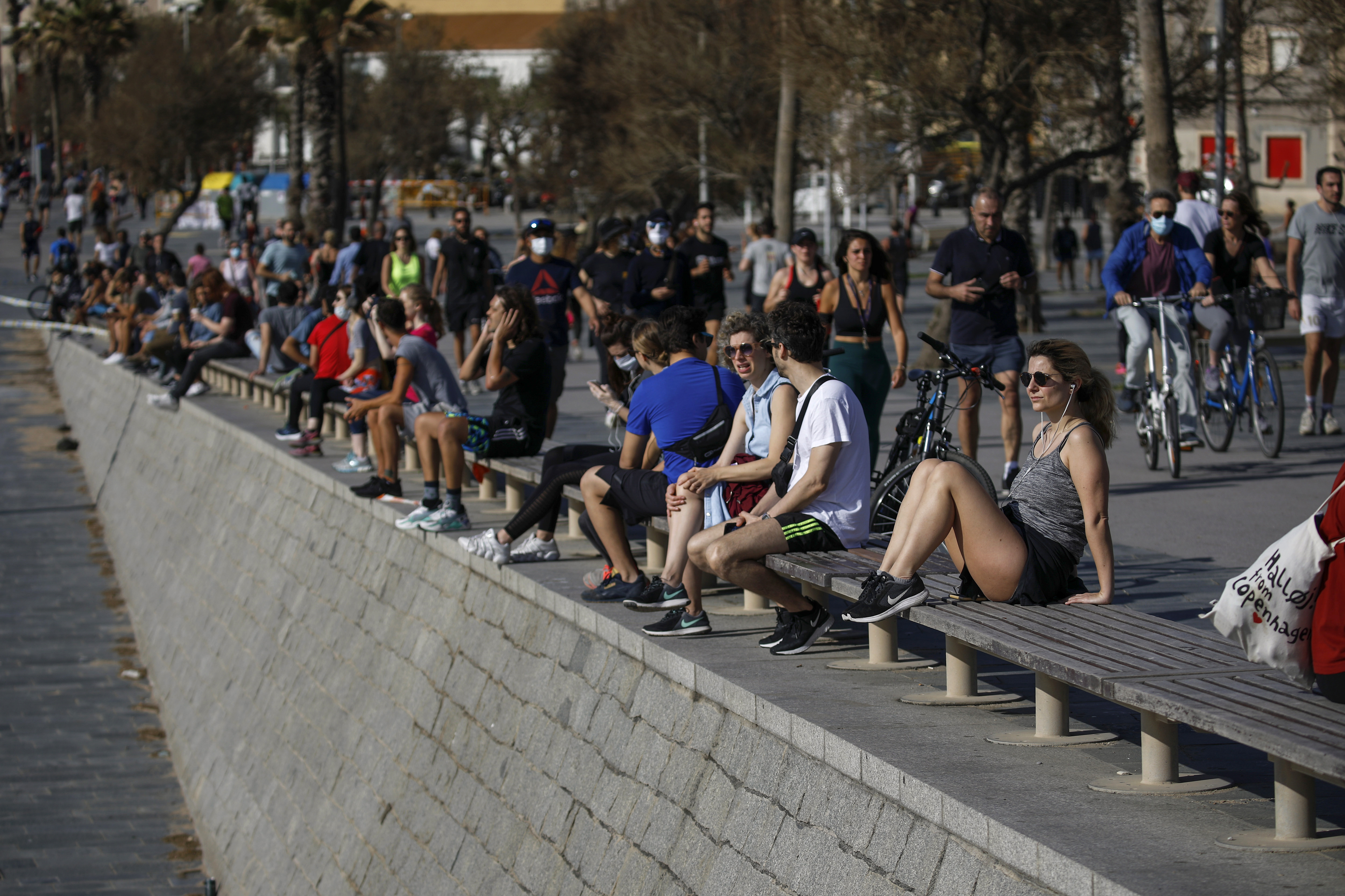 People sit as others exercising in a seafront promenade in this photo taken with a telephoto lens in Barcelona, Spain, Saturday, May 2, 2020. Spaniards have filled the streets of the country to do exercise for the first time after seven weeks of confinement in their homes to fight the coronavirus pandemic. People ran, walked, or rode bicycles under a brilliant sunny sky in Barcelona on Saturday, where many flocked to the maritime promenade to get as close as possible to the still off-limits beach. (Emilio Morenatti, AP Photo)