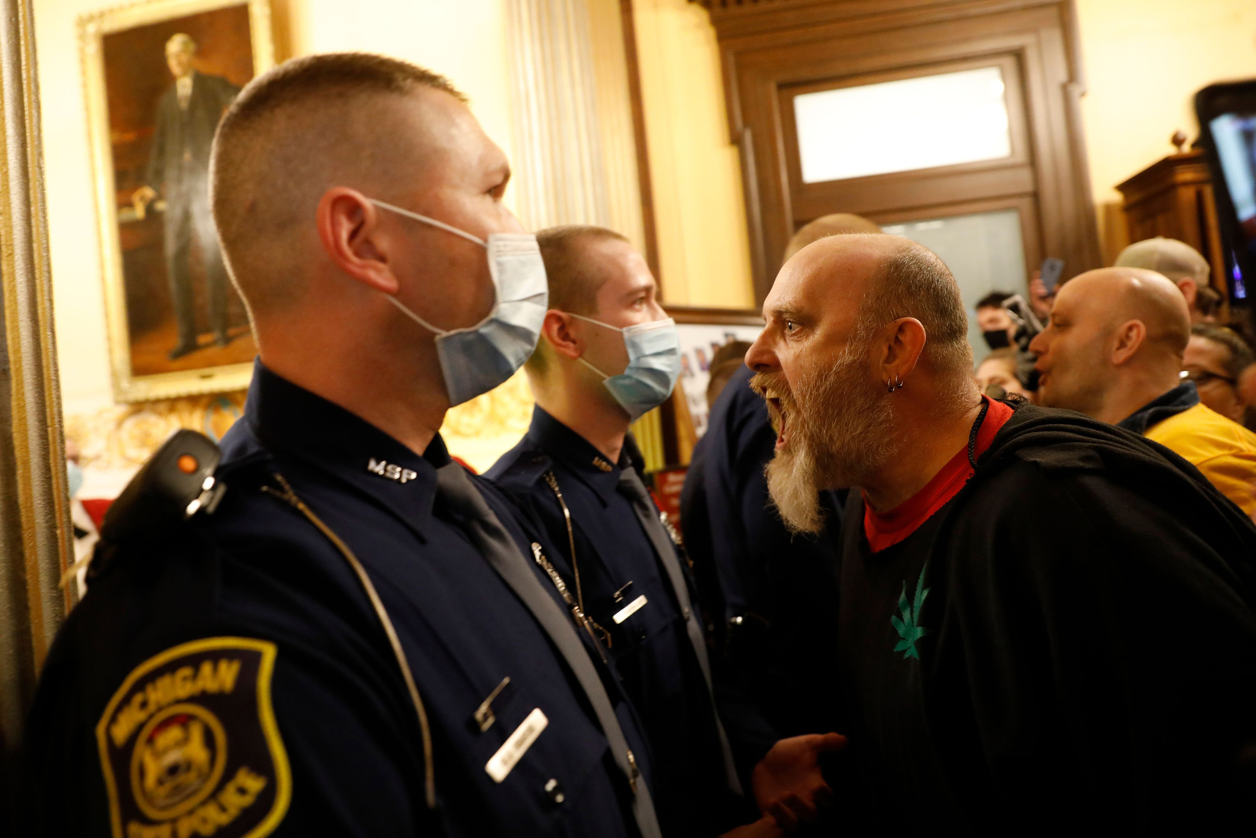 Unmasked protesters in Michigan try to enter the state's House of Representatives chamber but are blocked by masked Michigan State Police. (Photo: Jeff Kowalsky/AFP/Getty Images)