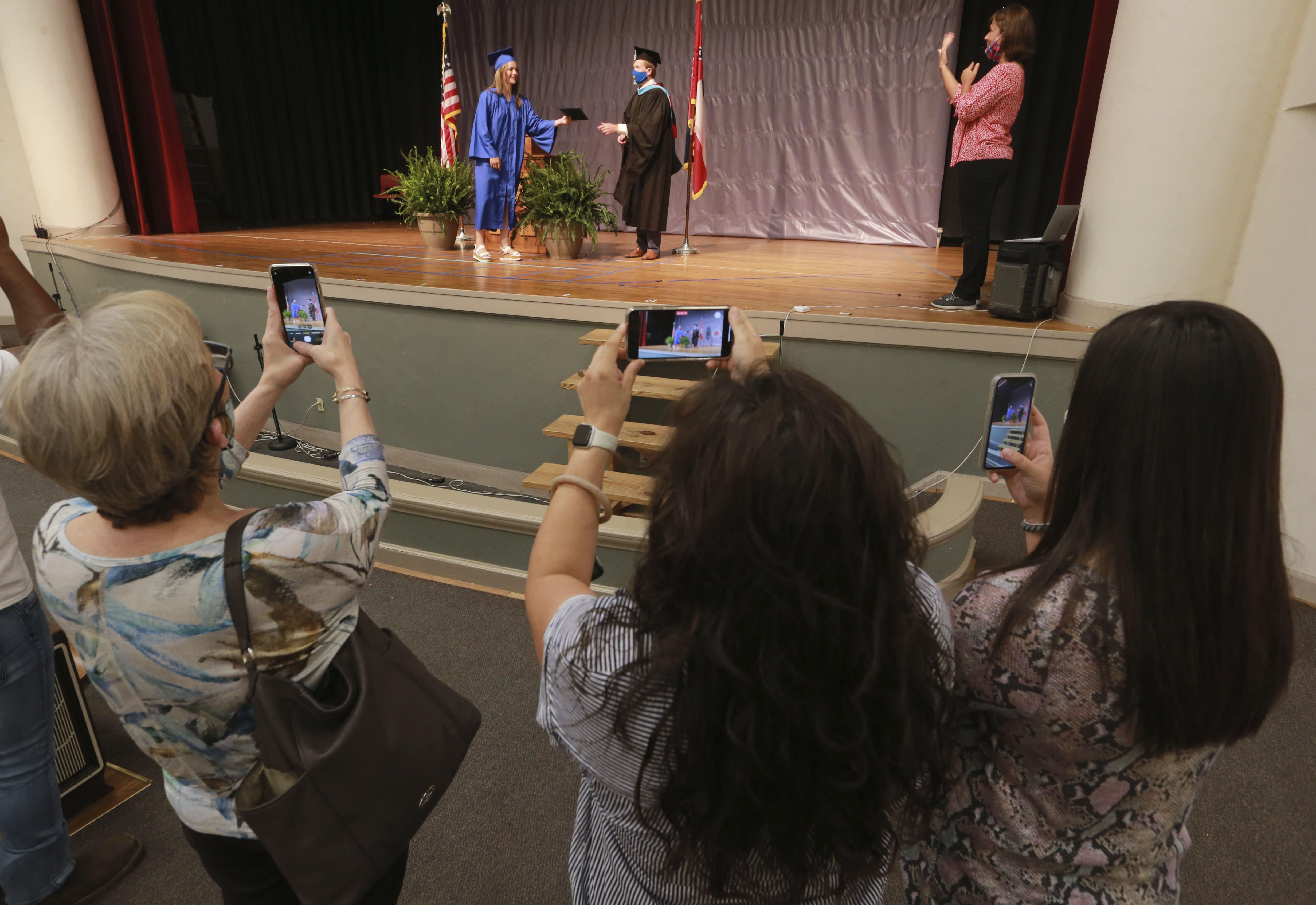 Family members watch Carmen Antillon receives her Tupelo High School diploma from Tupelo High School 12th grade Assistant Principal L.V. McNeal during a graduation ceremony at Milam Elementary School, Wednesday, May 6, 2020, in Tupelo Miss. The school district divided up the graduation ceremony to five different locations over three days with no more than four guests in attendance. (Thomas Wells/The Northeast Mississippi Daily Journal via AP)