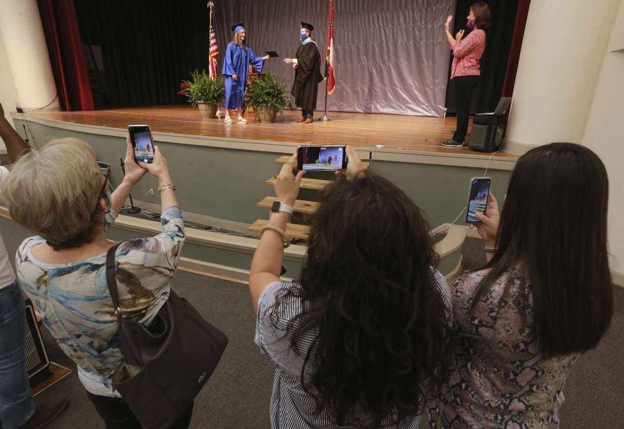 Family members watch Carmen Antillon receives her Tupelo High School diploma from Tupelo High School 12th grade Assistant Principal L.V. McNeal during a graduation ceremony at Milam Elementary School, Wednesday, May 6, 2020, in Tupelo Miss. The school district divided up the graduation ceremony to five different locations over three days with no more than four guests in attendance. (Thomas Wells/The Northeast Mississippi Daily Journal via AP)