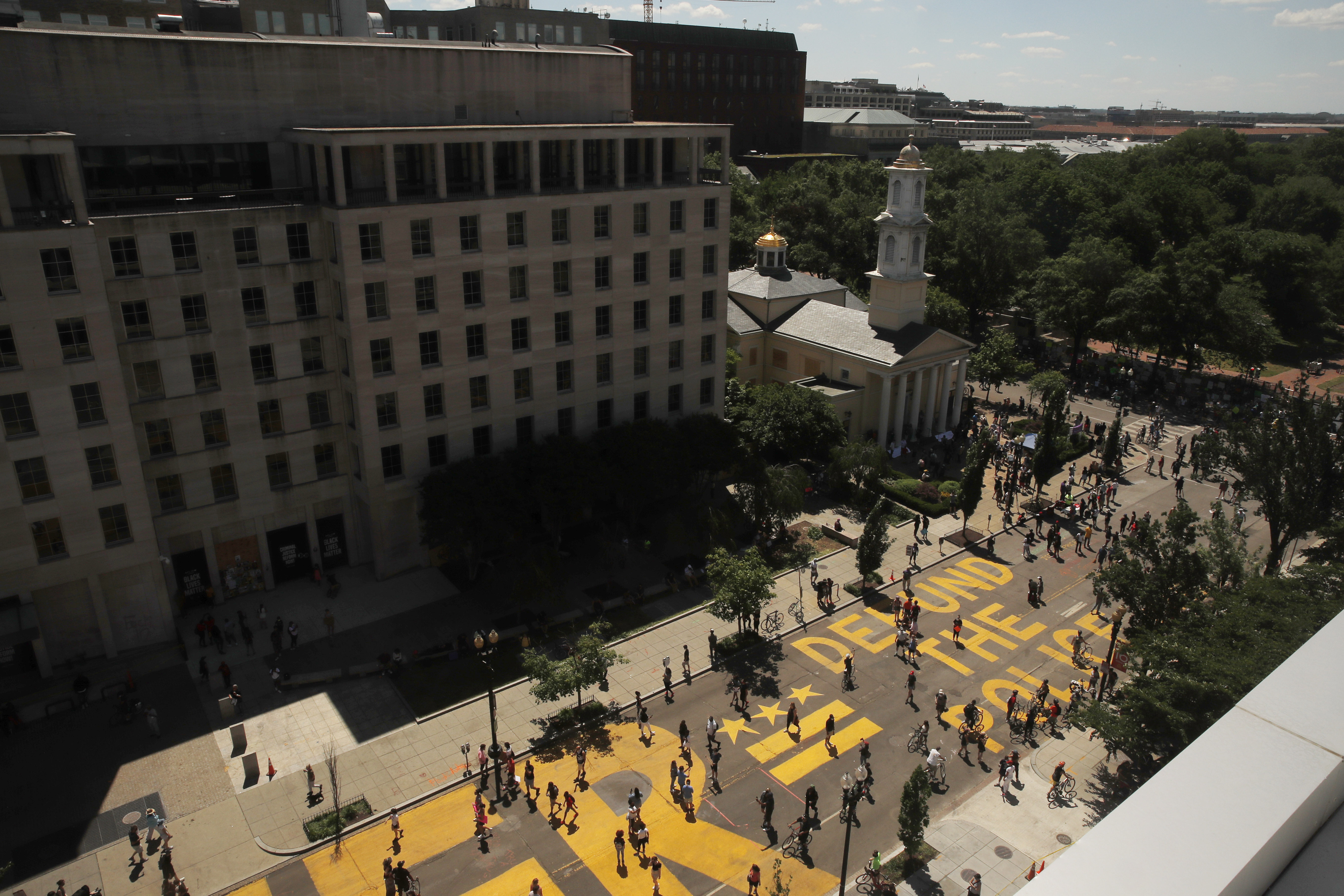 In this June 7, 2020, photo, people walk on the words 'defund the police' that was painted in bright yellow letters on 16th Street as demonstrators protest Sunday, June 7, 2020, near the White House in Washington, over the death of George Floyd, a black man who was in police custody in Minneapolis. (AP Photo/Maya Alleruzzo)