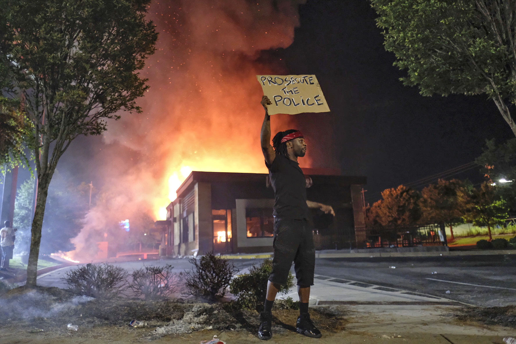 A person holds a sign as a Wendy's restaurant burns Saturday, June 13, 2020, in Atlanta after demonstrators allegedly set it on fire. (Ben Gray, Atlanta Journal-Constitution via AP)