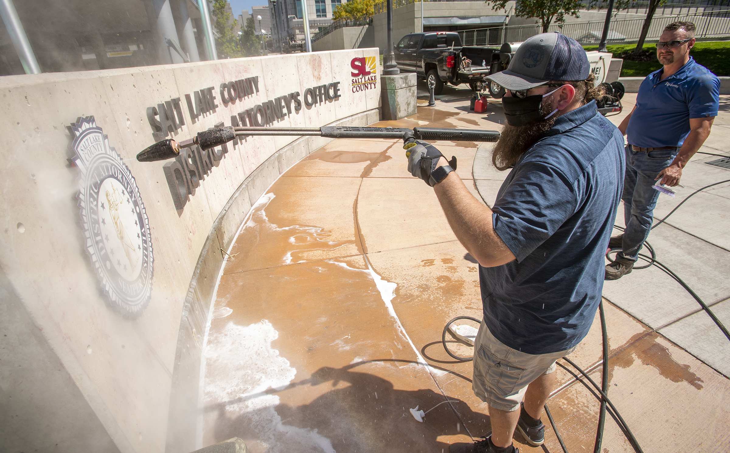 Chad Rasmussen, owner of Royce Industries, uses a pressure washer to clean paint from the sign in front of the Salt Lake County District Attorney’s Office building in Salt Lake City on Friday, July 10, 2020. The building suffered tens of thousands of dollars in damage when protesters broke out at least three windows and spread red paint over large portions of the building and area in front of the structure on Thursday. (Photo: Scott G Winterton, KSL)