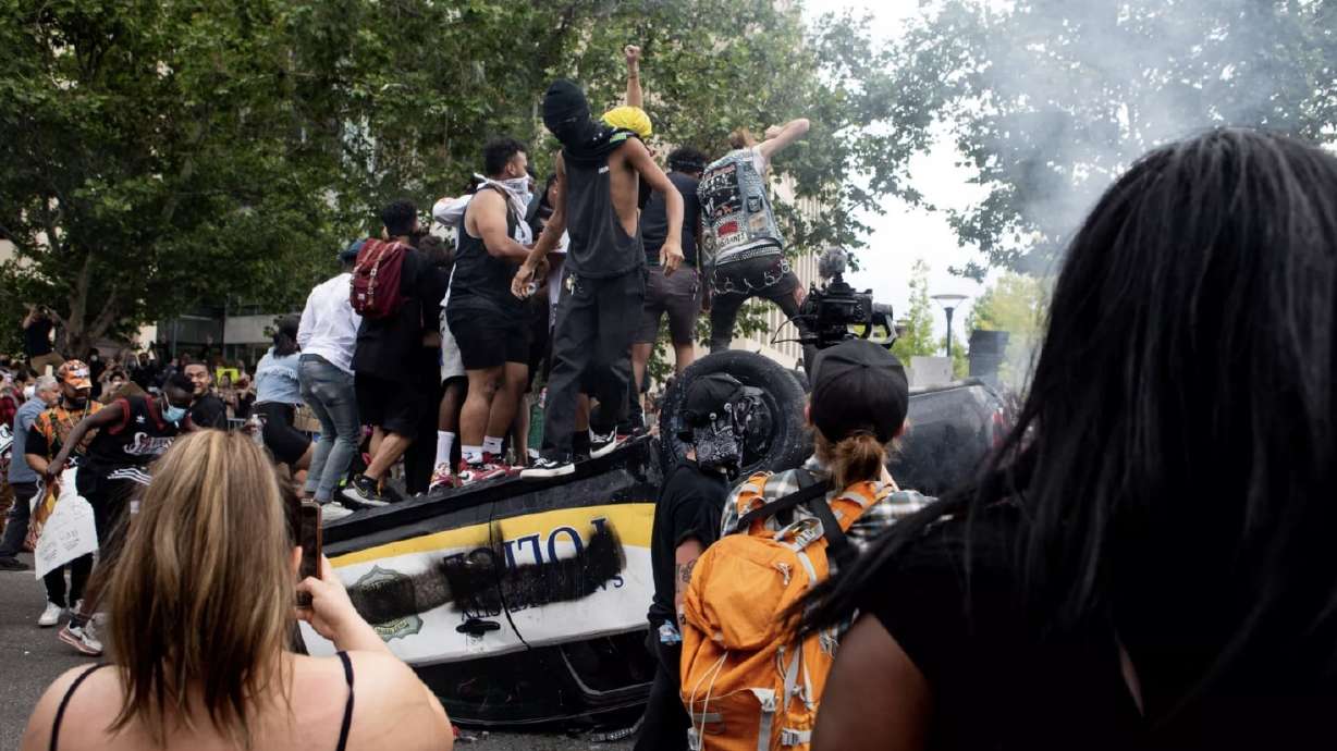 People jump on top of an overturned police car as they protest police brutality in Salt Lake City on Saturday, May 30, 2020.