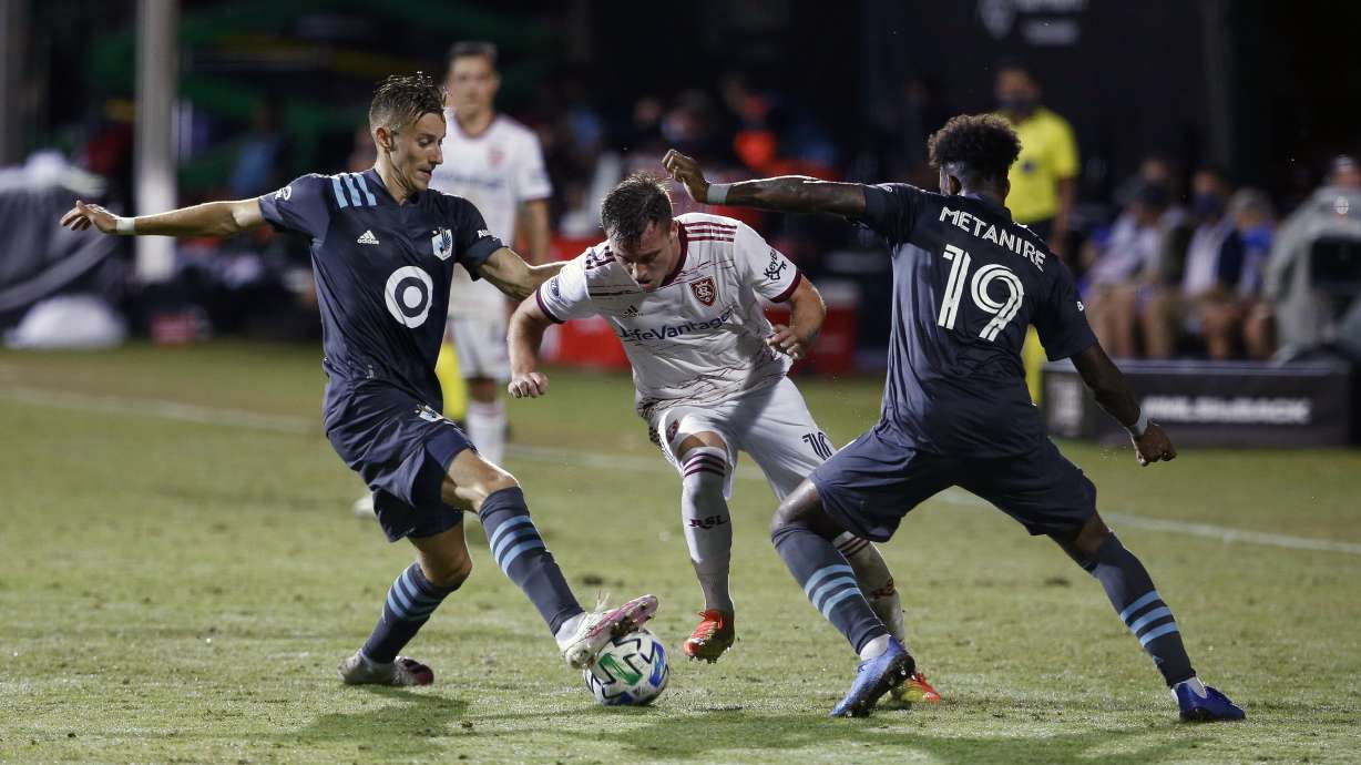 Real Salt Lake forward Corey Baird, middle, drives between Minnesota United defender Romain Metanire (19) and Minnesota United midfielder Jan Gregus (8) during the second half of an MLS soccer match in Kissimmee, Fla., early Saturday, July 18, 2020. (AP Photo/Reinhold Matay)
