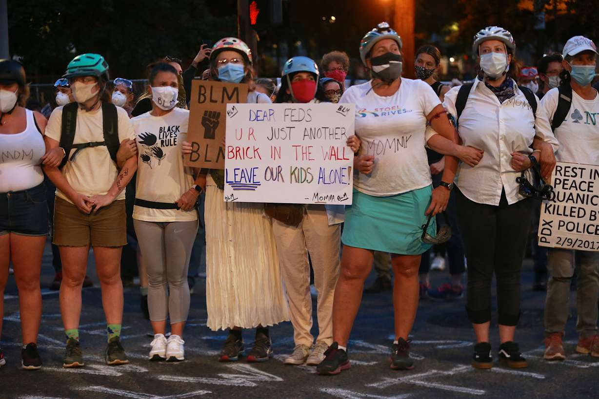 A group of mothers stand arm-in-arm outside the federal building and Justice Center in downtown Portland, Ore., on Saturday, July 18, 2020, during another night of protests in Portland. (Mark Graves, The Oregonian via AP)