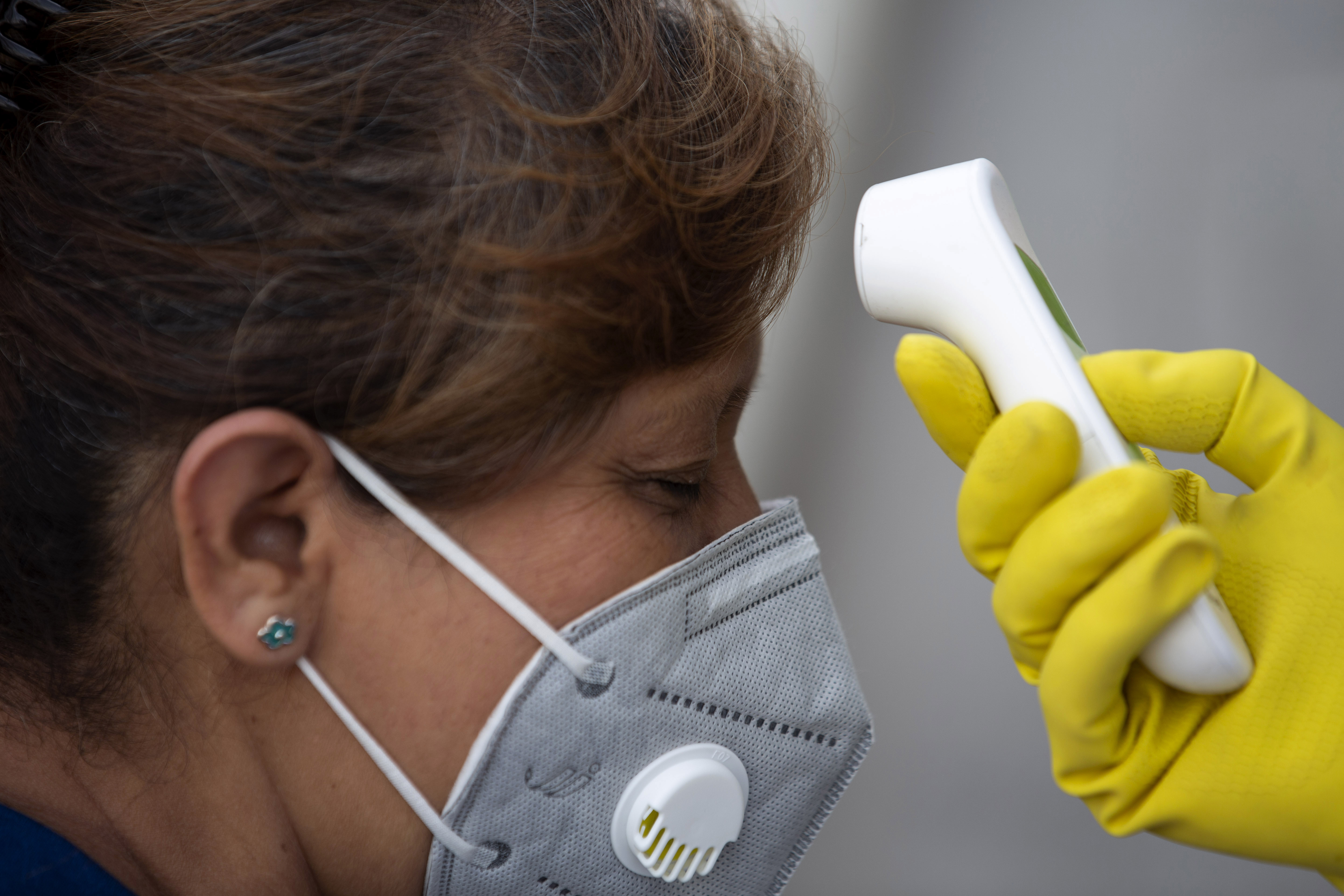 A health worker measures the temperature of a woman before allowing her to enter La Asuncion market to curb the spread of COVID-19 in Villa Nueva, Guatemala, Monday, July 20, 2020. (AP Photo/Moises Castillo) [Jul-20-2020]