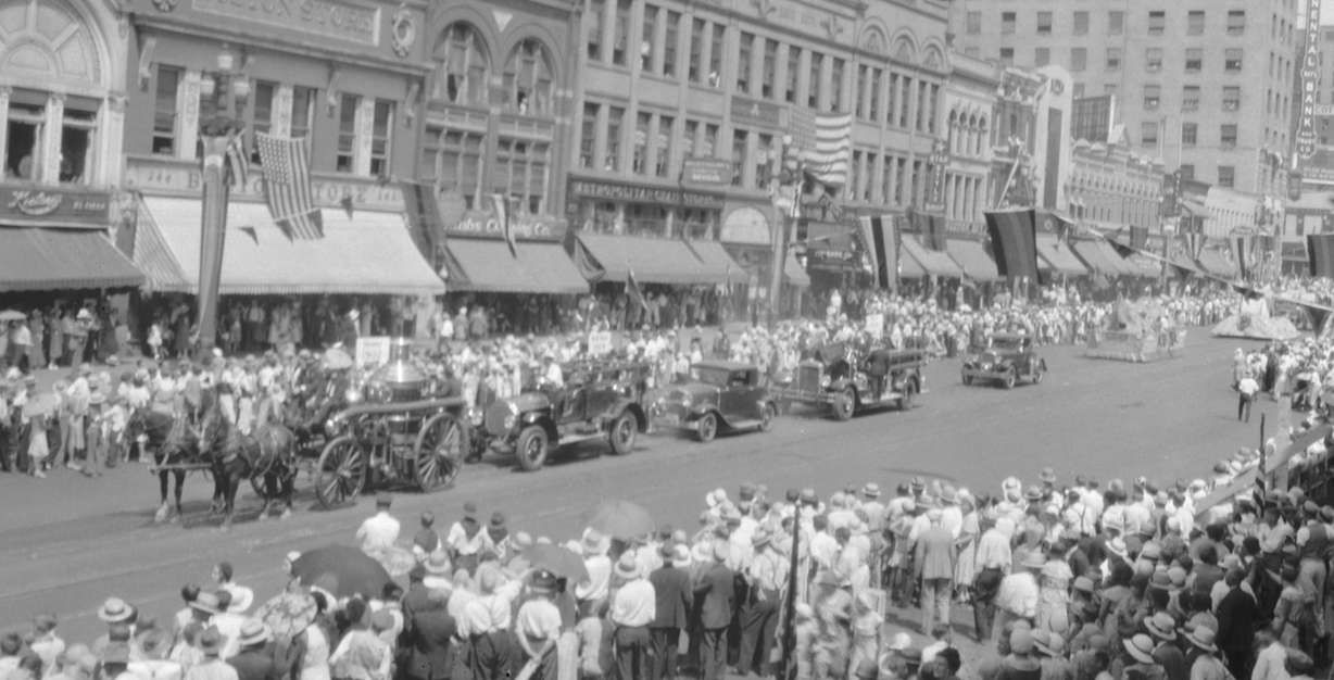 A wagon, cars, and floats traveling down Main Street Salt Lake City for a Pioneer Day parade in the 1930s.