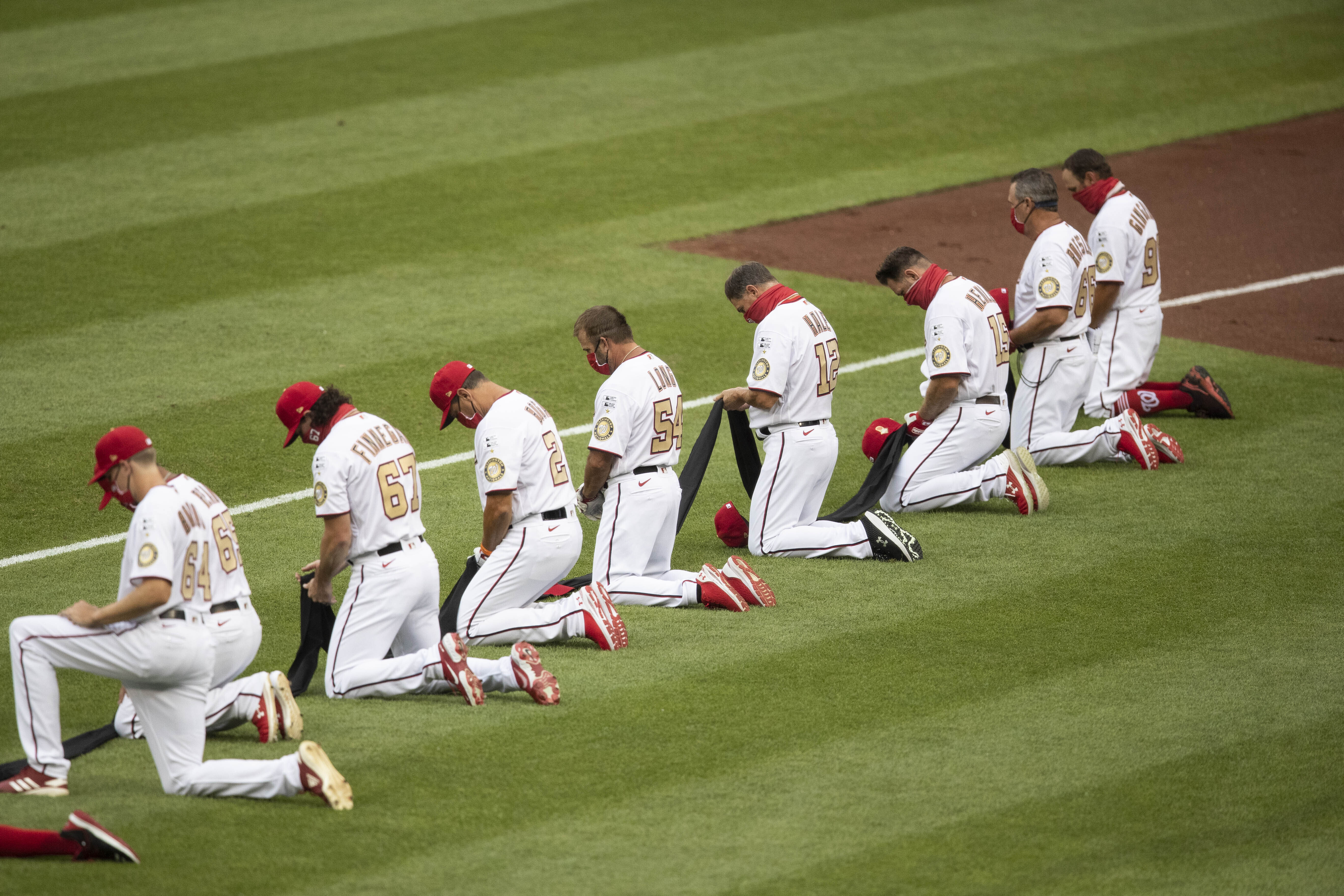 Members of Washington Nationals kneel and hold a piece of black fabric before an opening day baseball game against the New York Yankees at Nationals Park, Thursday, July 23, 2020, in Washington. (AP Photo/Alex Brandon)