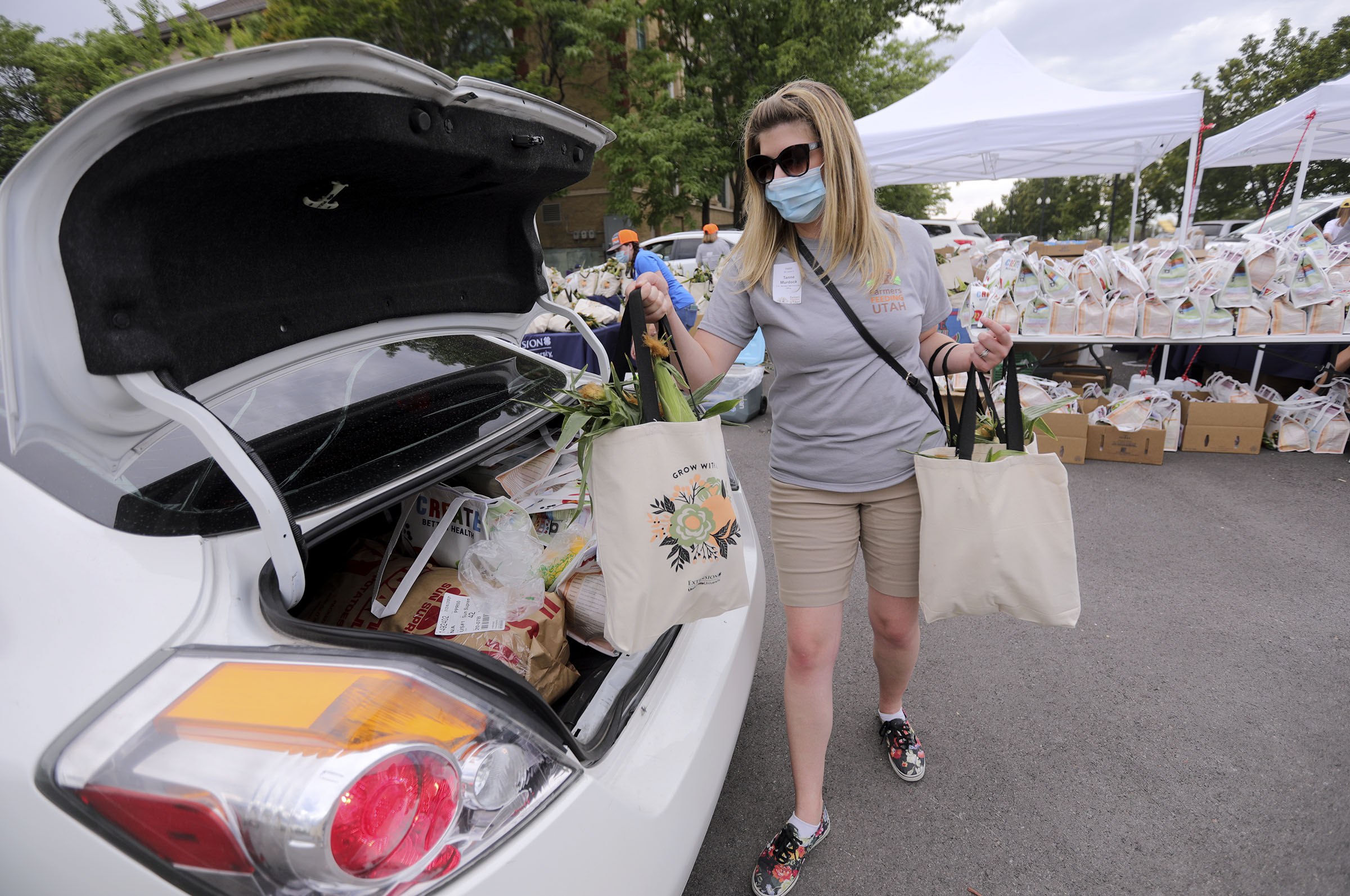 Tanne Murdock loads a bag of corn into a car as volunteers hand out donated food from Farmers Feeding Utah to those in need at the Utah State Fairpark in Salt Lake City on Monday, July 27, 2020.