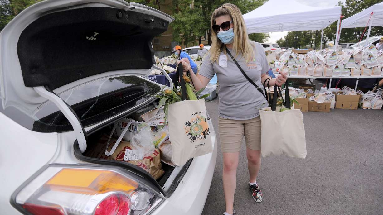Tanne Murdock loads a bag of corn into a car as volunteers hand out donated food from Farmers Feeding Utah to those in need at the Utah State Fairpark in Salt Lake City on Monday, July 27, 2020.
