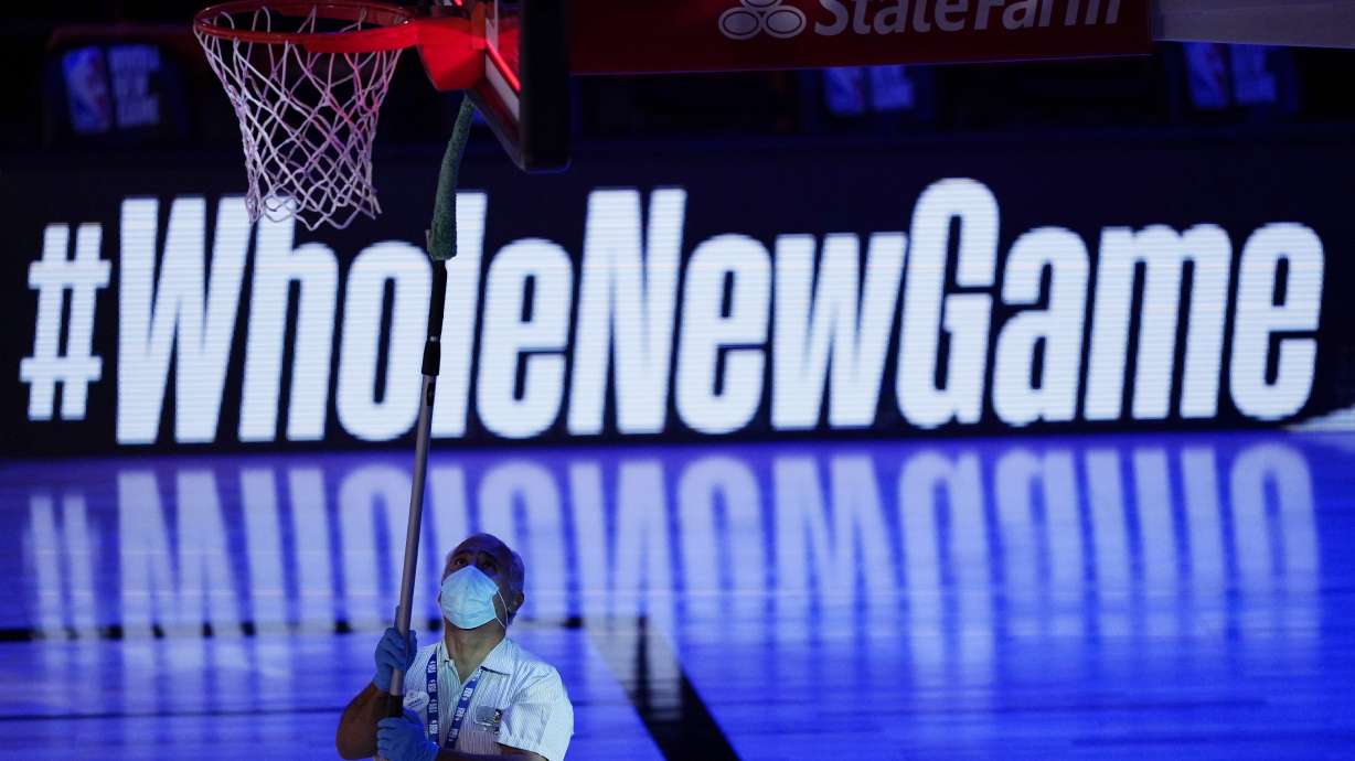 A worker cleans a backboard after an NBA basketball game between the Utah Jazz and the Oklahoma City Thunder, Saturday, Aug. 1, 2020, in Lake Buena Vista, Fla.