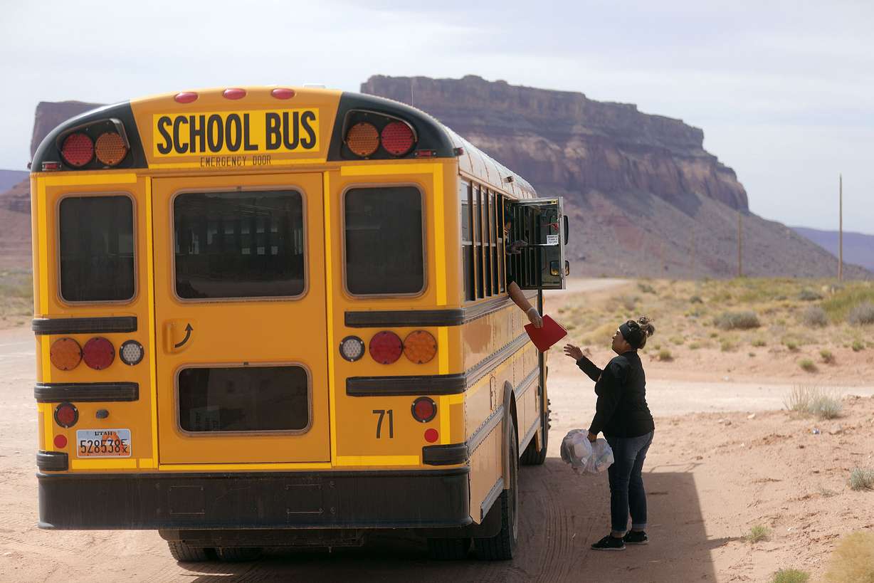 Cara Luna, Tse’bii’nidzisgai Elementary School fourth grade teacher, hands homework to Tiffany Chee, who is picking up food and homework for her three kids as well as neighbors in Oljato-Monument Valley, San Juan County, on Thursday, April 30, 2020. School staff prepare the food bags and help bus drivers deliver the meals and homework on their regular bus route two days a week while schools are closed due to the COVID-19 pandemic. The Navajo Nation has one of the highest per capita COVID-19 infection rates in the country.