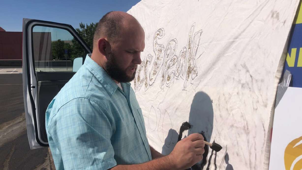 Robert Briggs paints “JO20.com” on a cloth taped to the side of a van with “#LetHerSpeak” on it as a part of a Libertarian convoy protest, St. George, Utah, Aug. 8, 2020