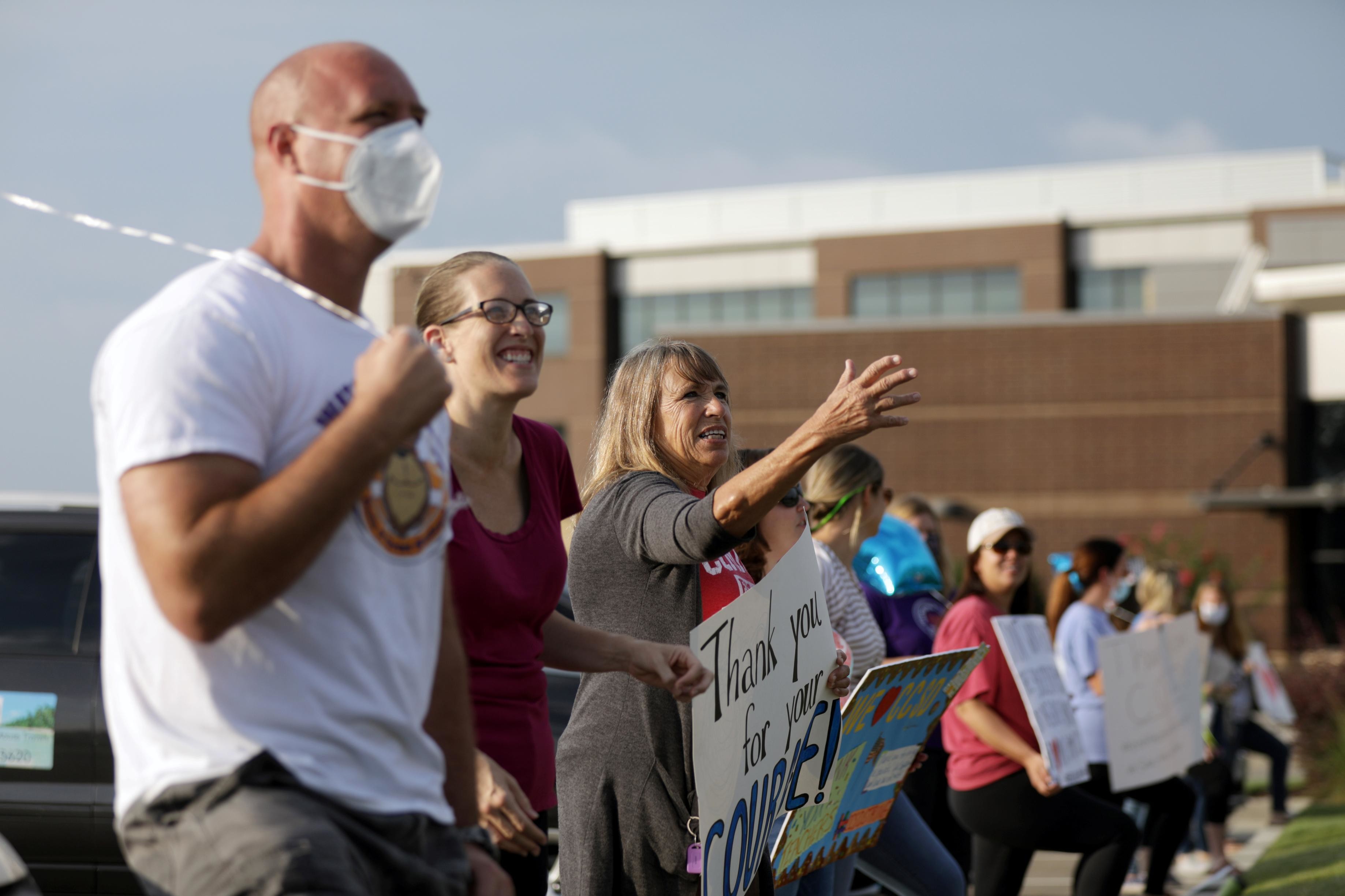 Supporters of the Cherokee County School District's decision to reopen schools cheer on faculty arriving to the district's headquarters in Canton, Georgia.