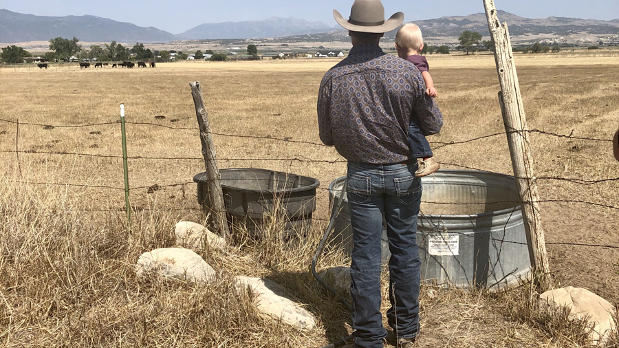 Alex Wight holds his son, Cinch, while filling a trough with water for their cows.