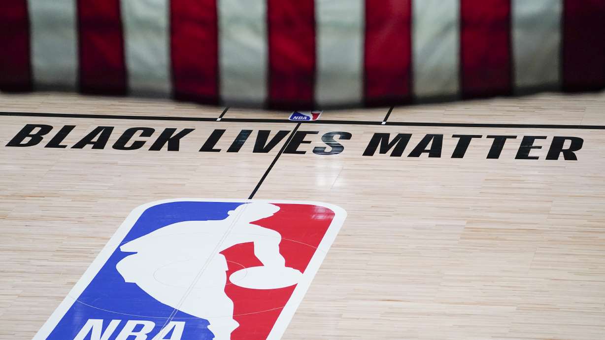 Black Lives Matter is displayed near the NBA logo in an empty basketball arena Friday, Aug. 28, 2020, in Lake Buena Vista, Fla. The NBA playoffs will resume Saturday after the league and the National Basketball Players Association detailed the commitments that made players comfortable continuing the postseason. In a joint statement released Friday, the sides say they will immediately establish a social justice coalition, made up of players, coaches and owners, that would focus on issues such as voting access and advocating for meaningful police and criminal justice reform. (AP Photo/Ashley Landis, Pool)