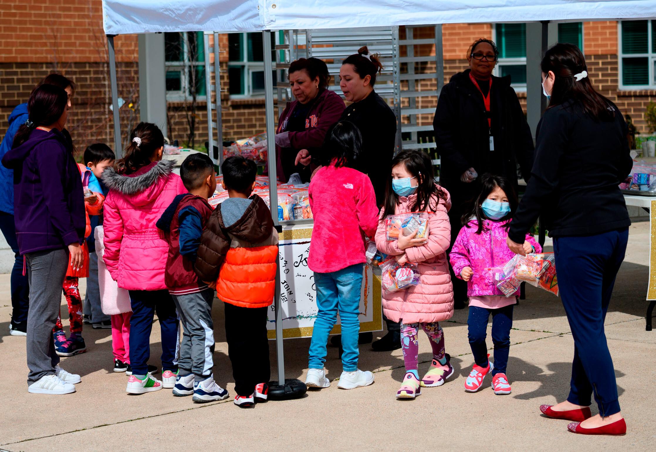 Children can carry coronavirus in their noses and throats for weeks even if they don't show any symptoms. This image shows children, some wearing face masks as a preventive measure, picking up free lunch at Kenmore Middle School in Arlington, Virginia on March 16, 2020.