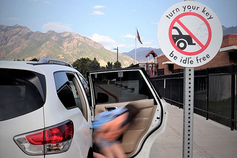 A girl is dropped off next to a sign reminding people to turn off their vehicles while they’re parked. 