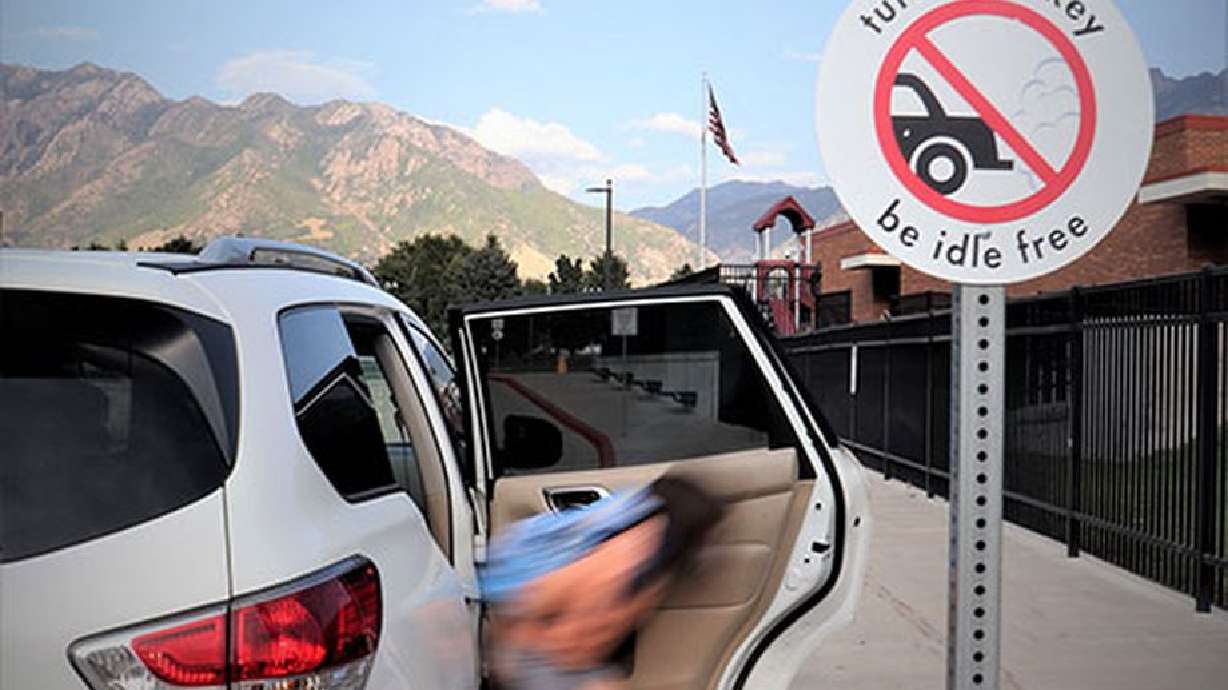 A girl is dropped off next to a sign reminding people to turn off their vehicles while they’re parked.