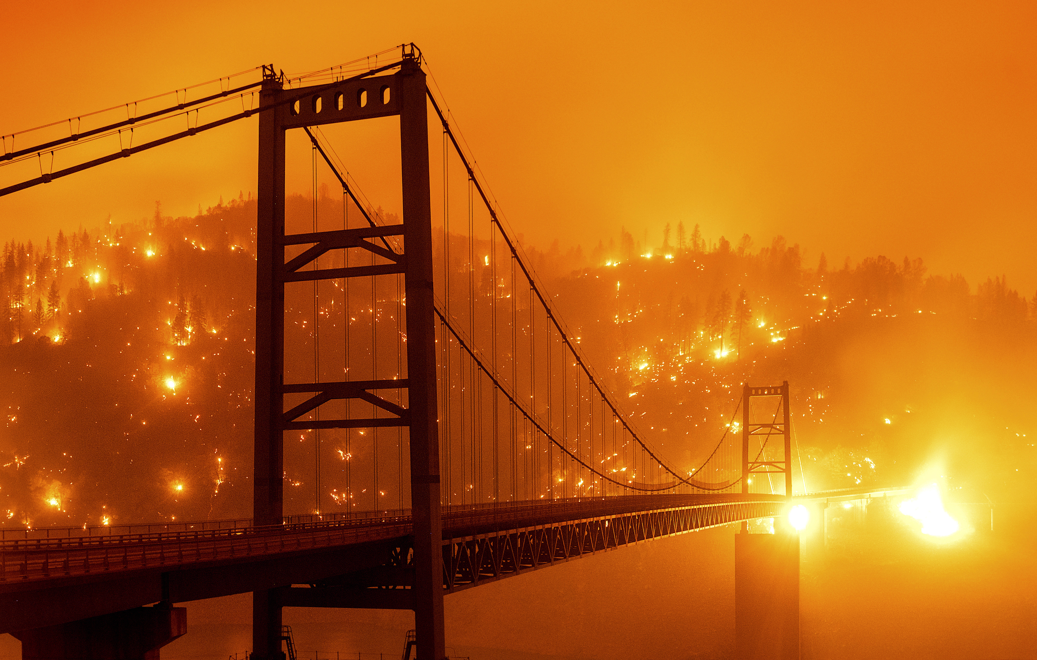 In this Sept. 9, 2020, file photo, taken with a slow shutter speed, embers light up a hillside behind the Bidwell Bar Bridge as the Bear Fire burns in Oroville, Calif. Two unusual weather phenomena combined to create some of the most destructive wildfires the West Coast states have seen in modern times.