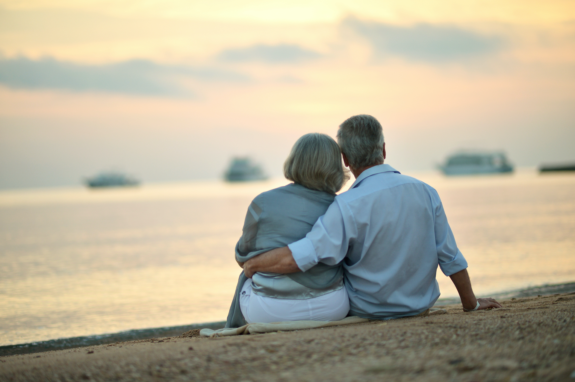 Happy Mature older couple relaxing on beach at sunset,back view