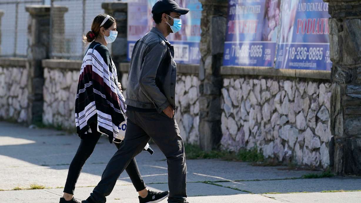 Two people wear protective face masks as they walk along a commercial street in the Gravesend section of the Brooklyn borough of New York on September 28, 2020.
