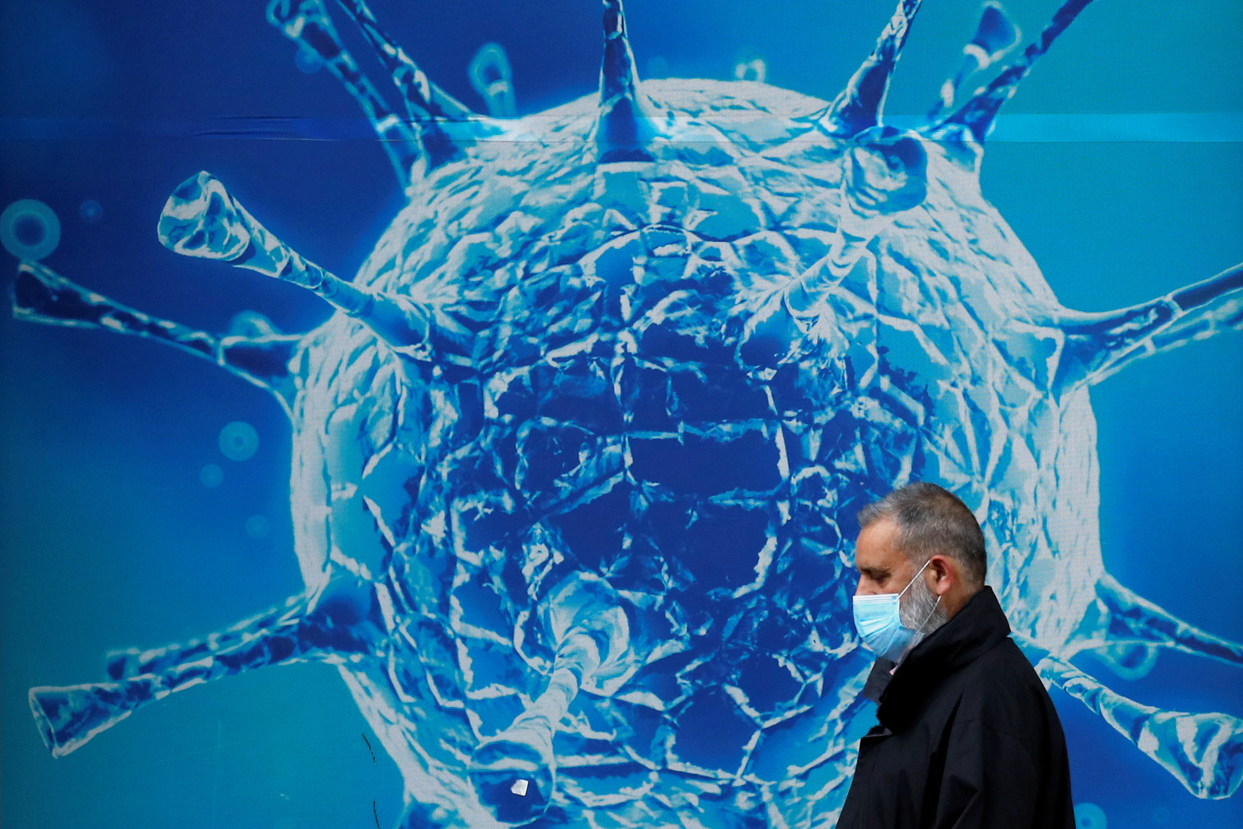 FILE PHOTO: A man wearing a protective face mask walks past an illustration of a virus outside a regional science centre, as the city and surrounding areas face local restrictions in an effort to avoid a local lockdown being forced upon the region, amid the coronavirus disease (COVID-19) outbreak, in Oldham, Britain Aug. 3, 2020.